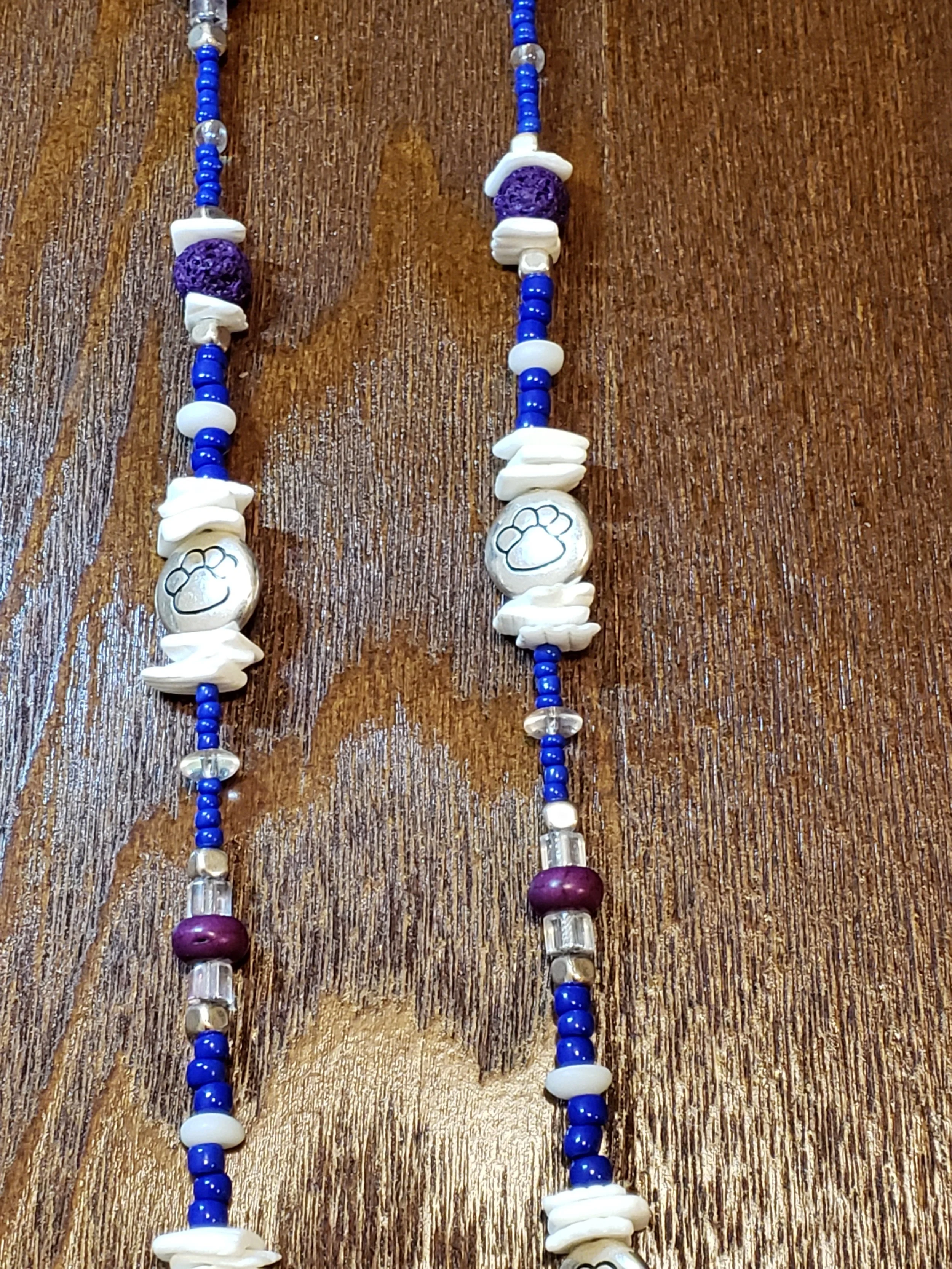 Beaded necklaces with white, blue, purple, and clear beads and paw print charms on a wooden surface.