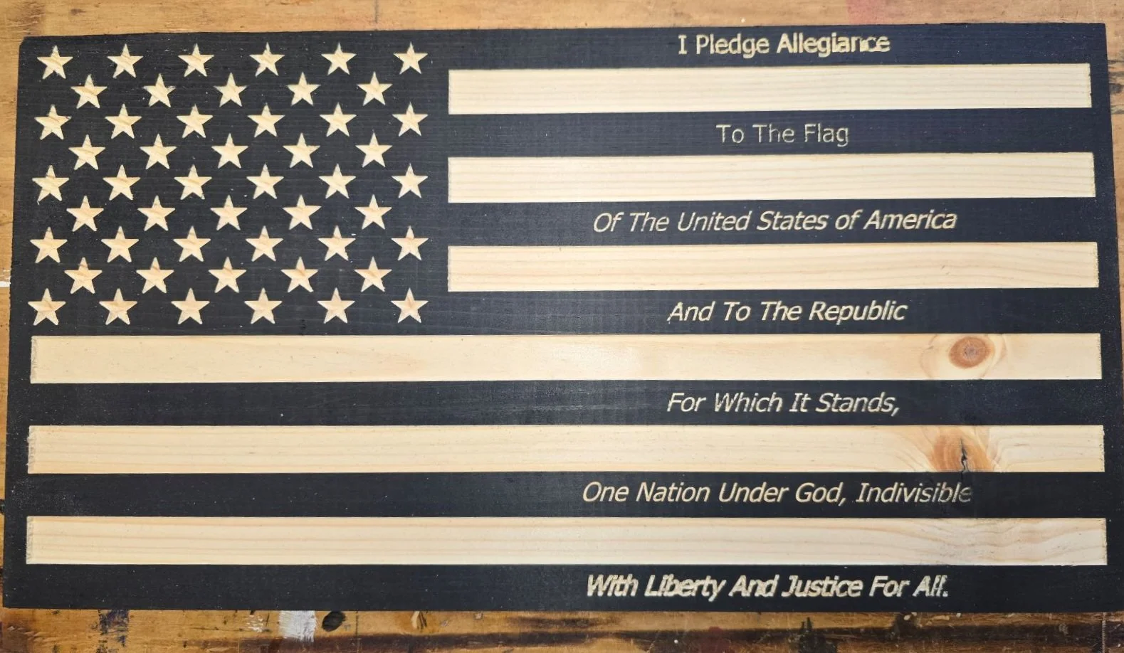 Decorative wooden American flag with 50 stars in the canton and stripes, featuring a pledge of allegiance inscribed across the stripes.