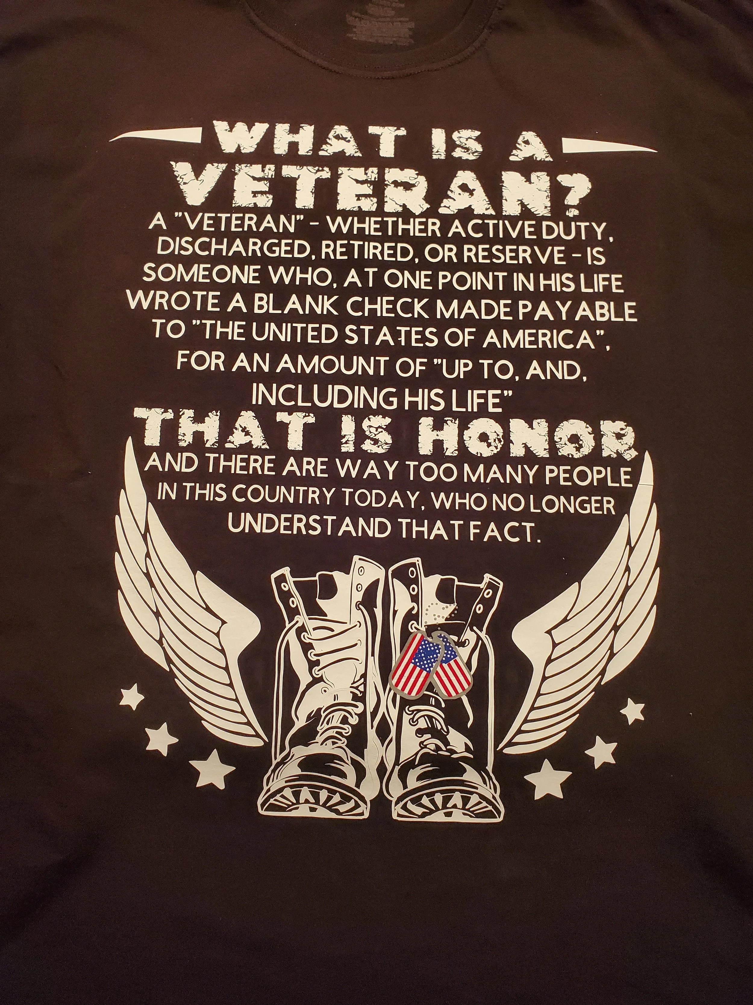 A T-shirt with a quote about veterans and military service, featuring a graphic of combat boots with angel wings and dog tags with American flags.