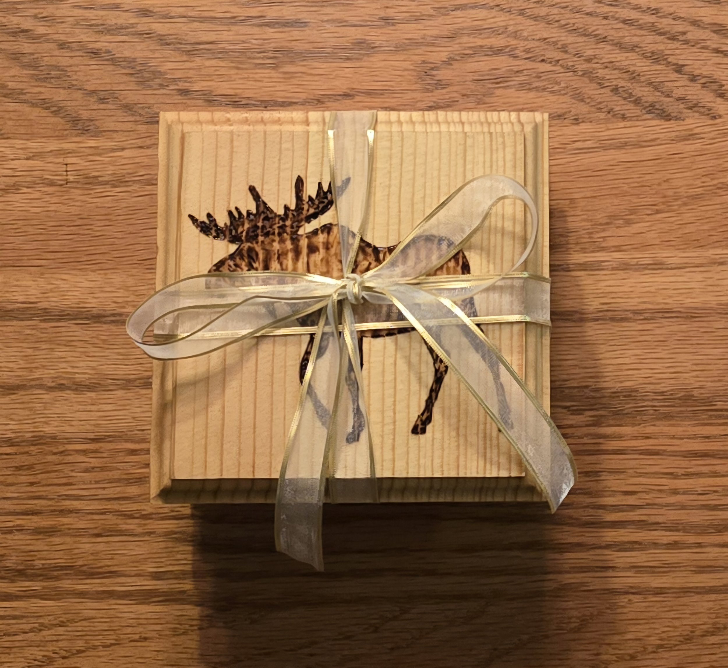 A gift box with a deer illustration on the lid, tied with a transparent ribbon bow, placed on a wooden surface.