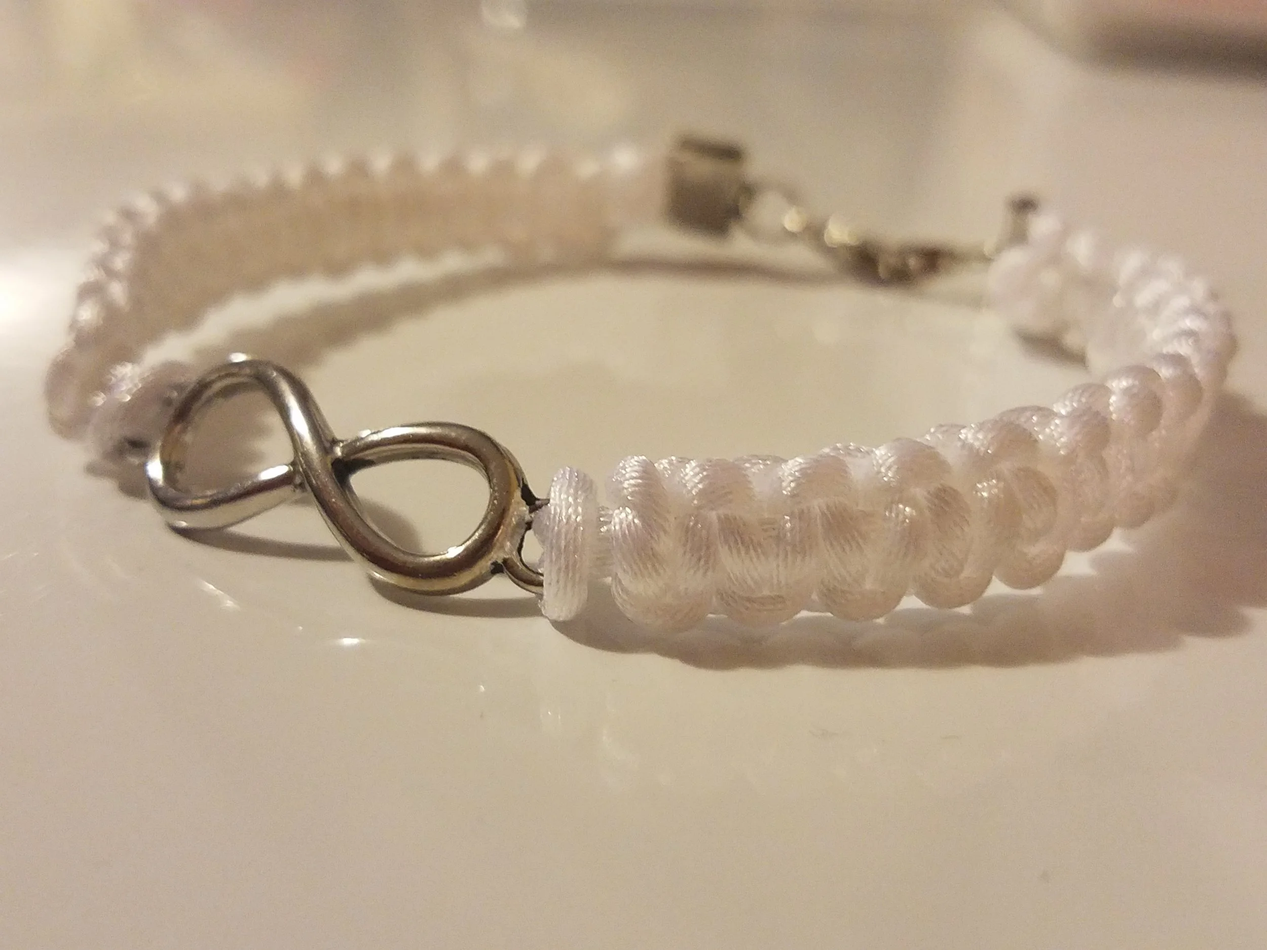 A close-up of a white beaded bracelet with a silver heart-shaped charm on a light surface.