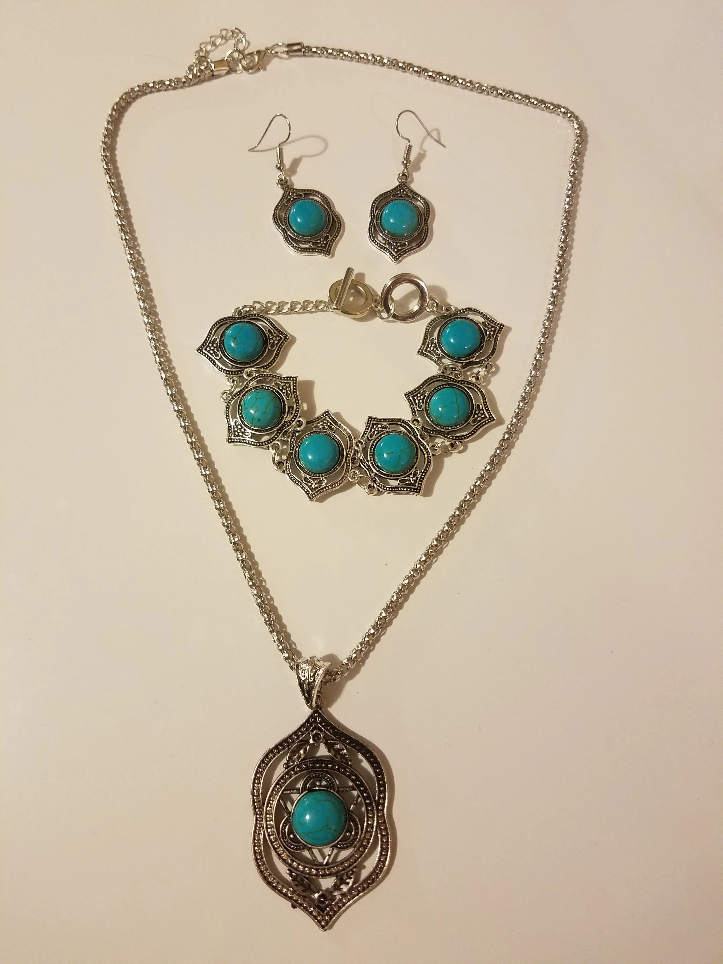 Silver jewelry set with turquoise stones, including a necklace, bracelet, and earrings displayed on a white background.