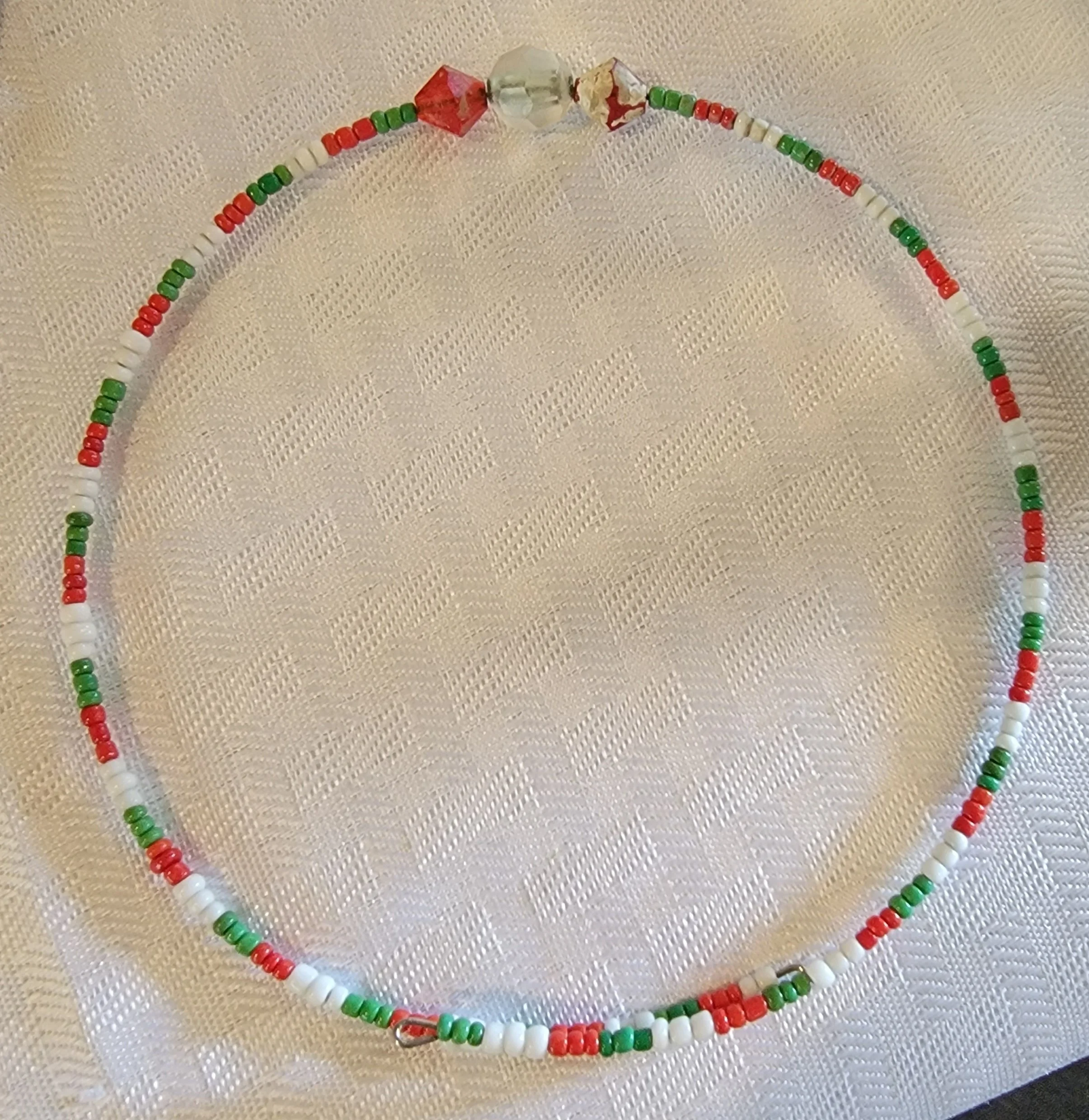Beaded necklace with white, red, and green beads laid flat on a textured, cream-colored surface.