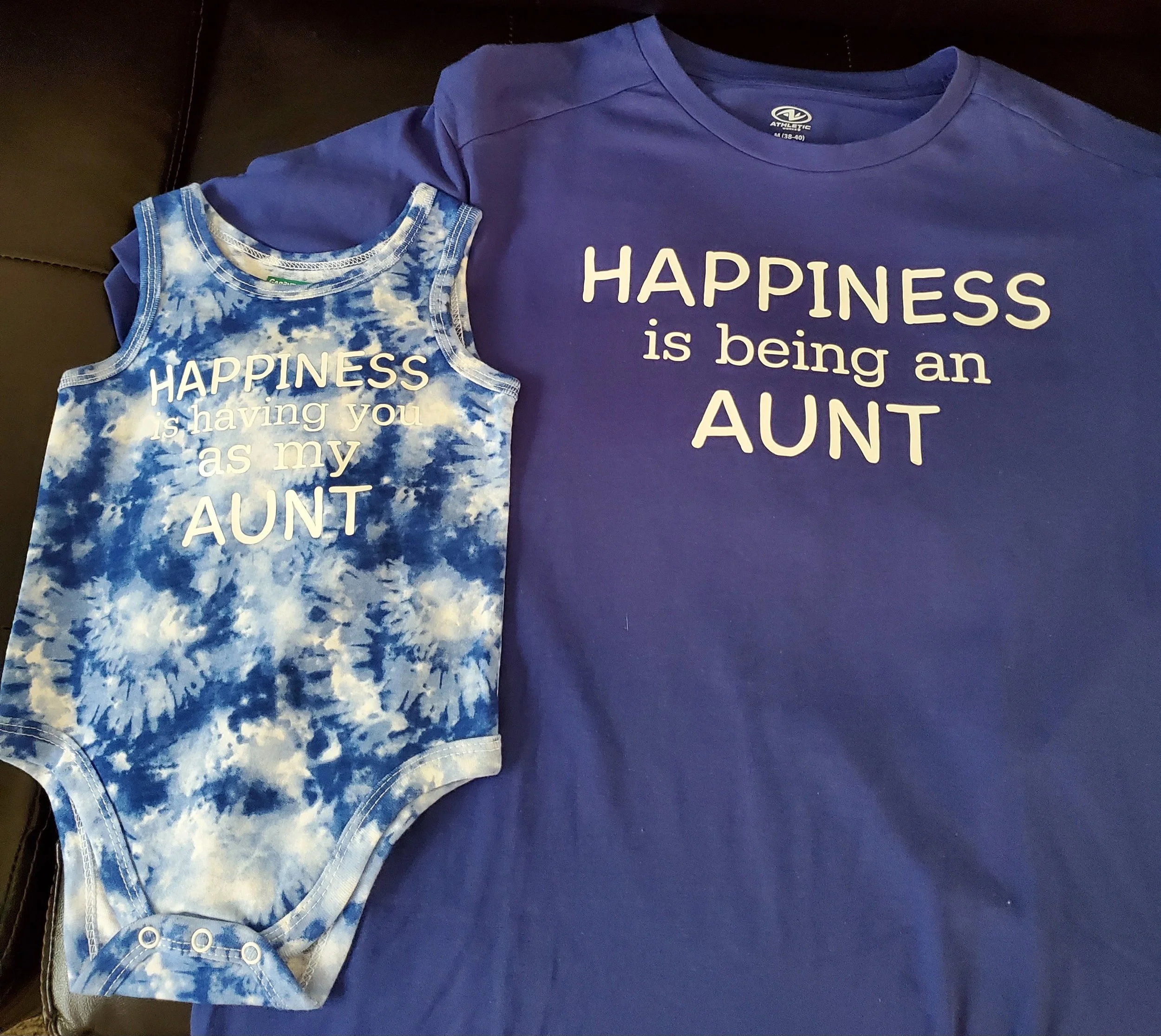 Matching blue shirts with white text that says, "HAPPINESS is being an AUNT." The smaller shirt has a tie-dye pattern, while the larger shirt is plain.