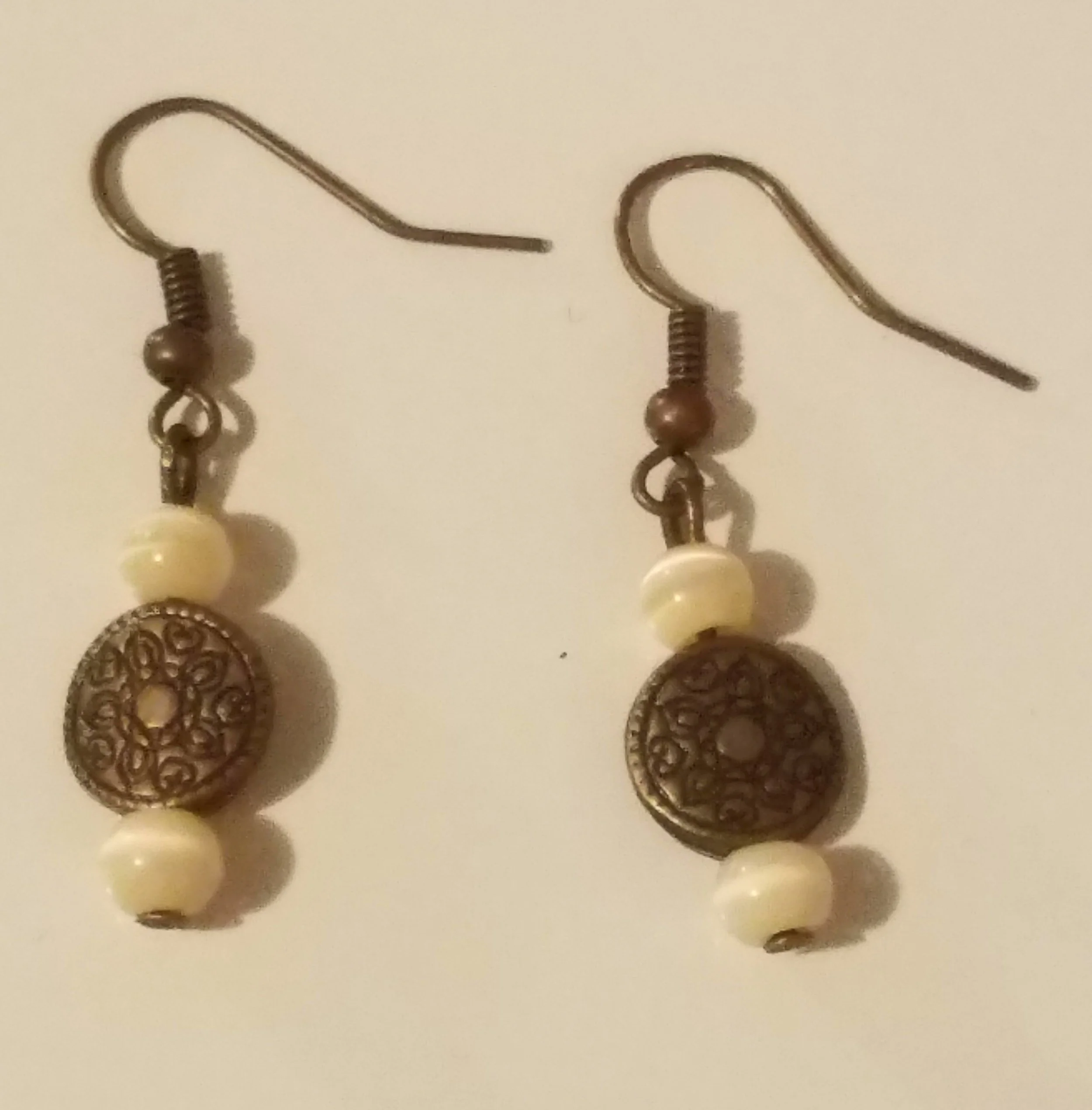 Pair of earrings with metal hook, cream beads, and ornate metal disc charms.