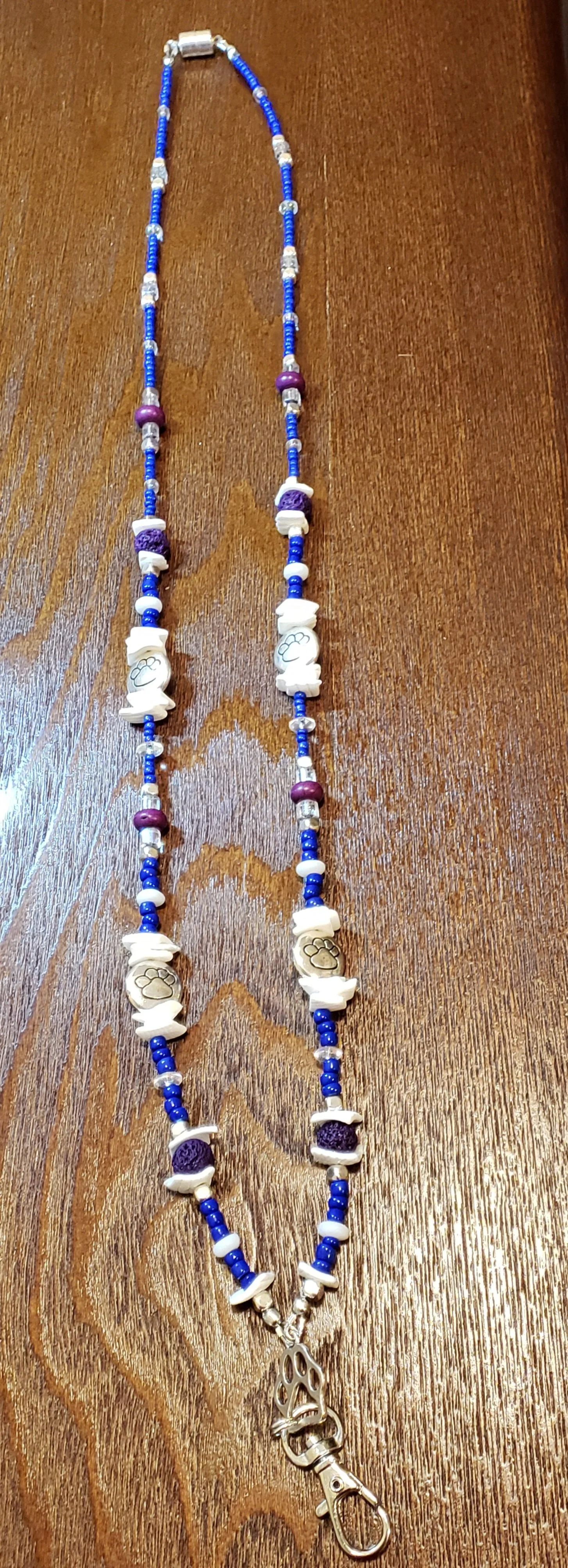 A beaded necklace with blue, purple, white, and clear beads, featuring white paw print charms.