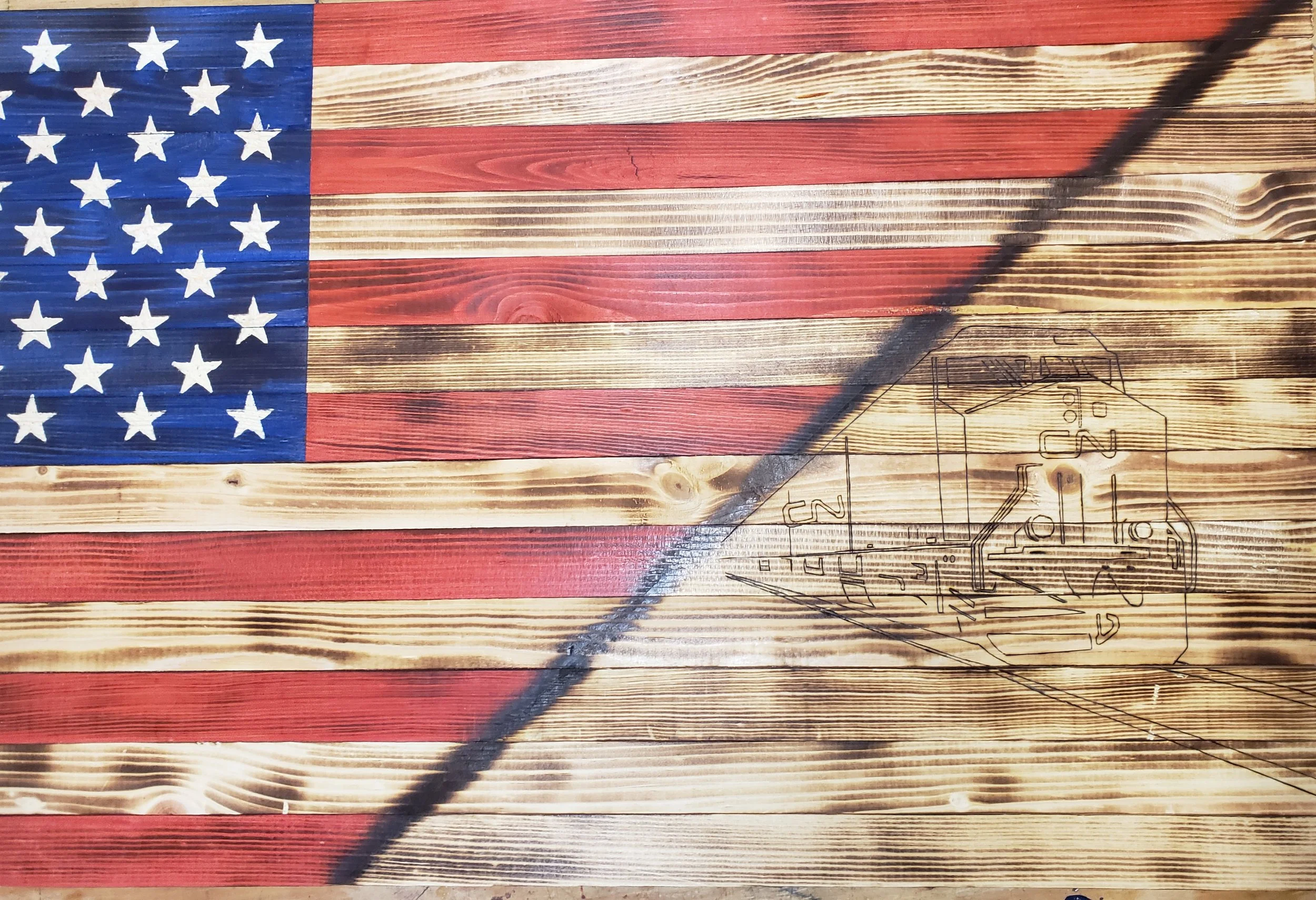 American flag painted on wood with a line drawing of a train engine in the lower right corner.