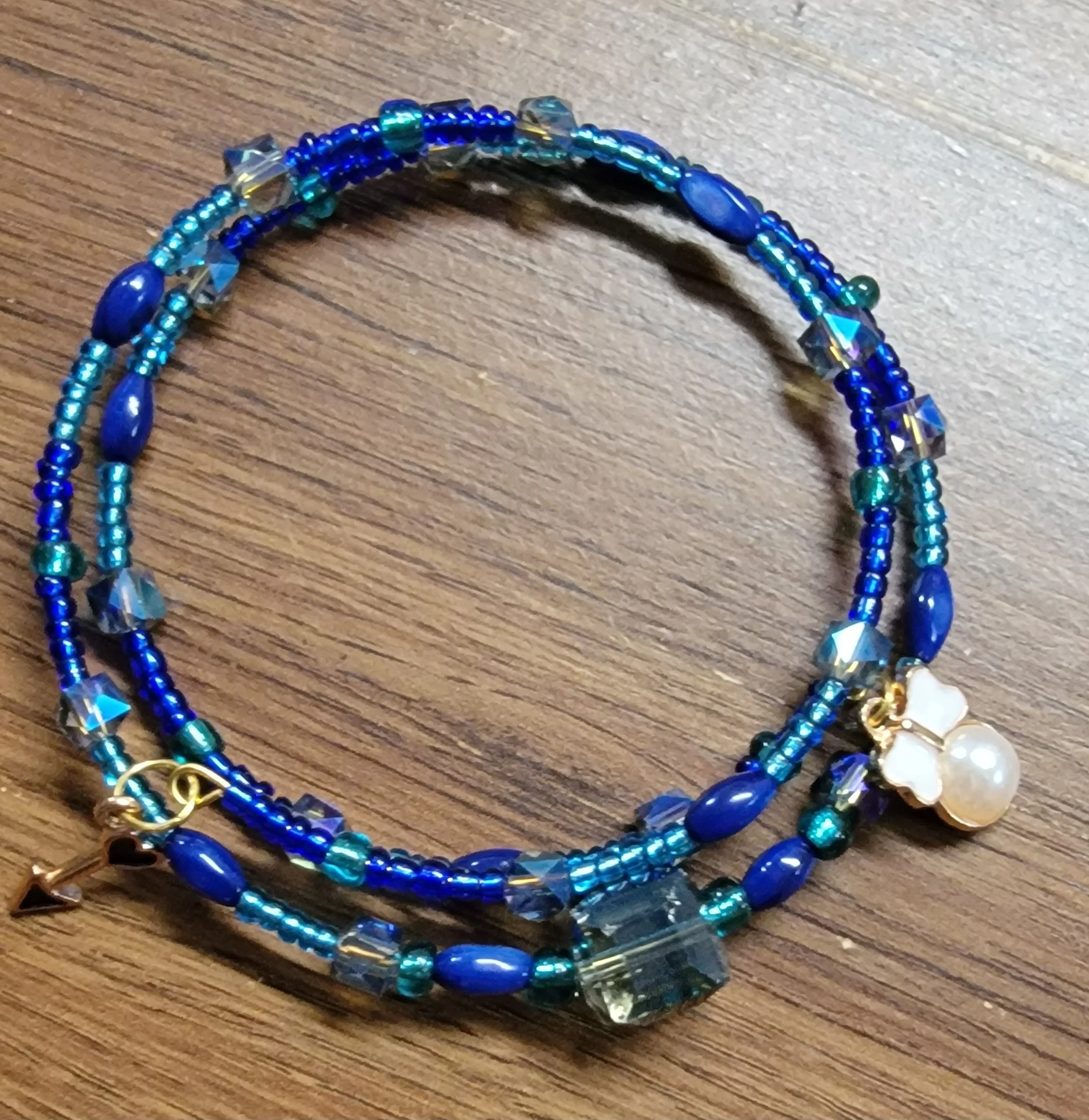 Stacked blue beaded bracelets with a white flower and pearl charm on a wooden surface.