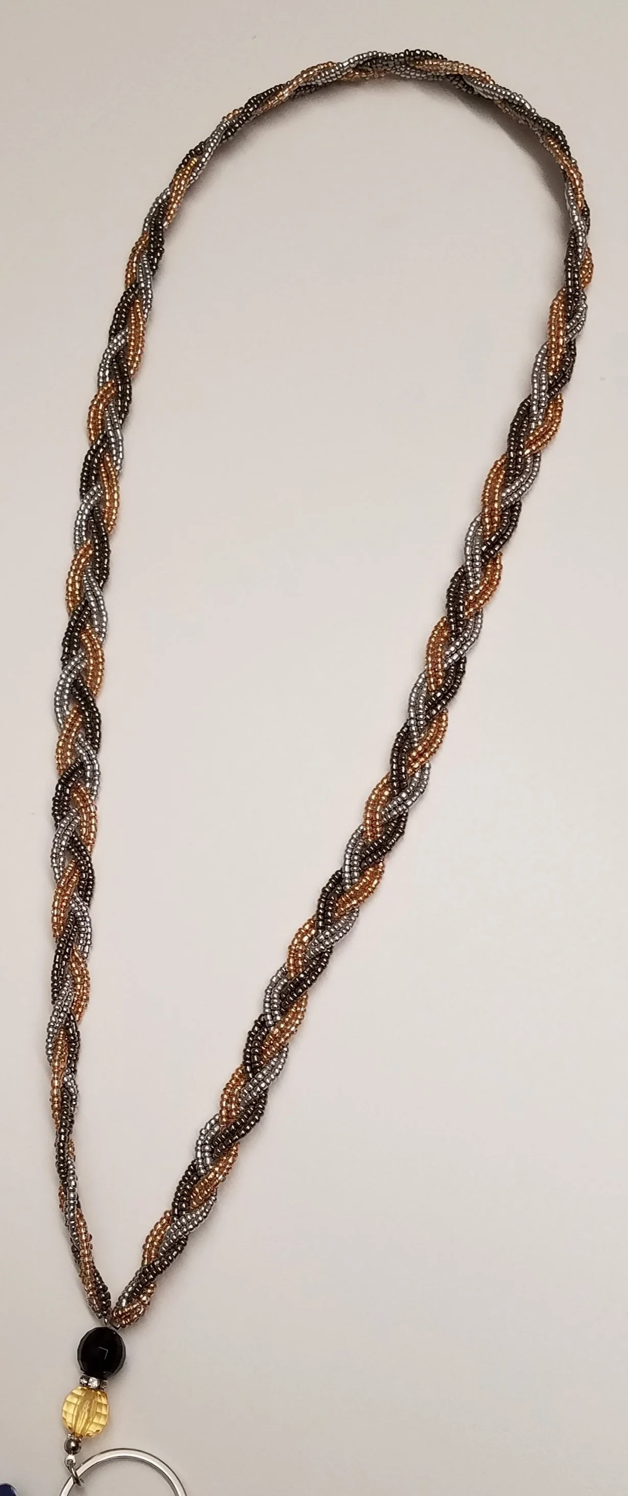 A beaded necklace with a black, gold, and silver bead pendant, hanging against a plain white background.
