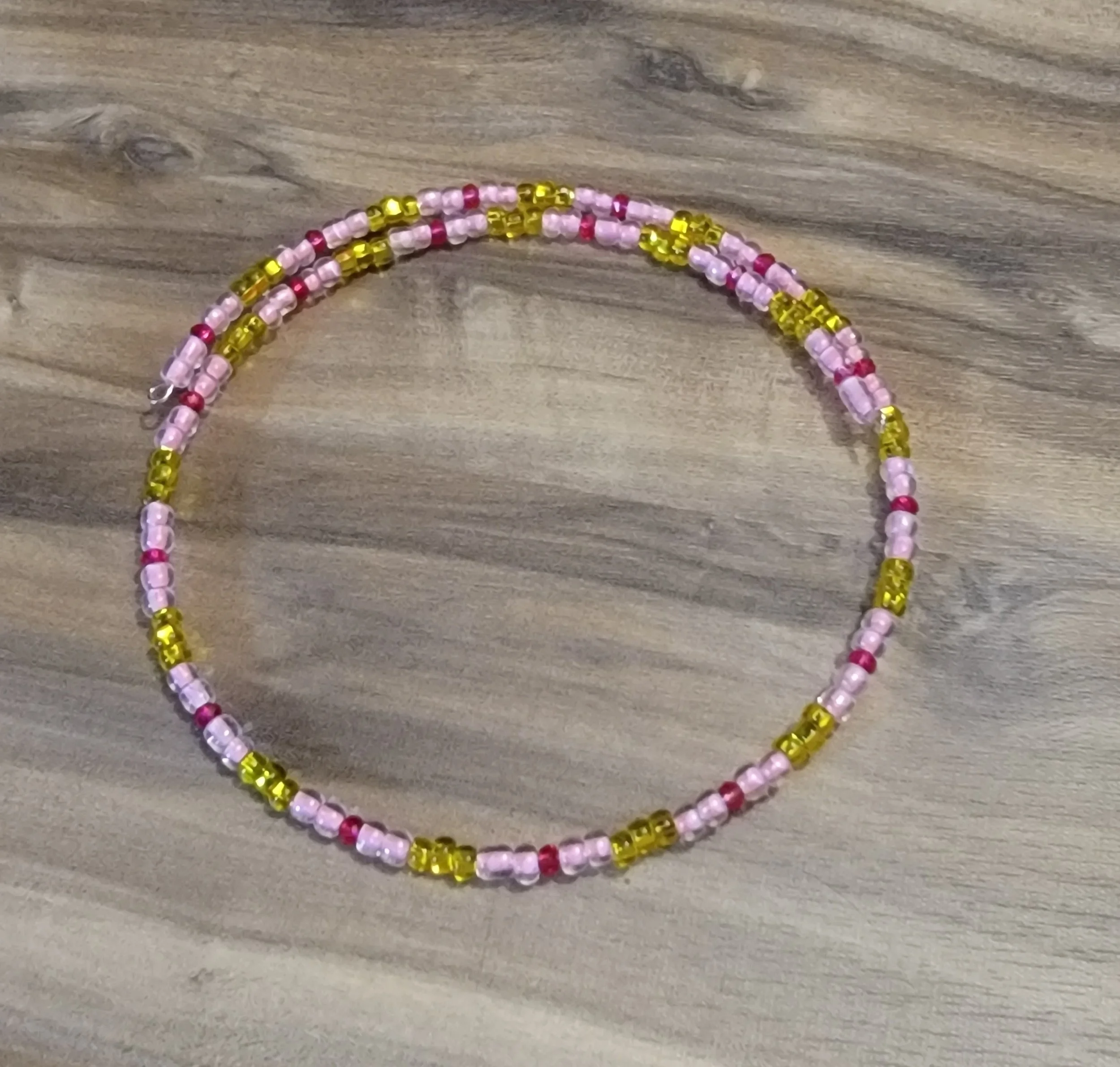 Colorful beaded bracelet on a wooden surface, made of pink, yellow, and red beads.
