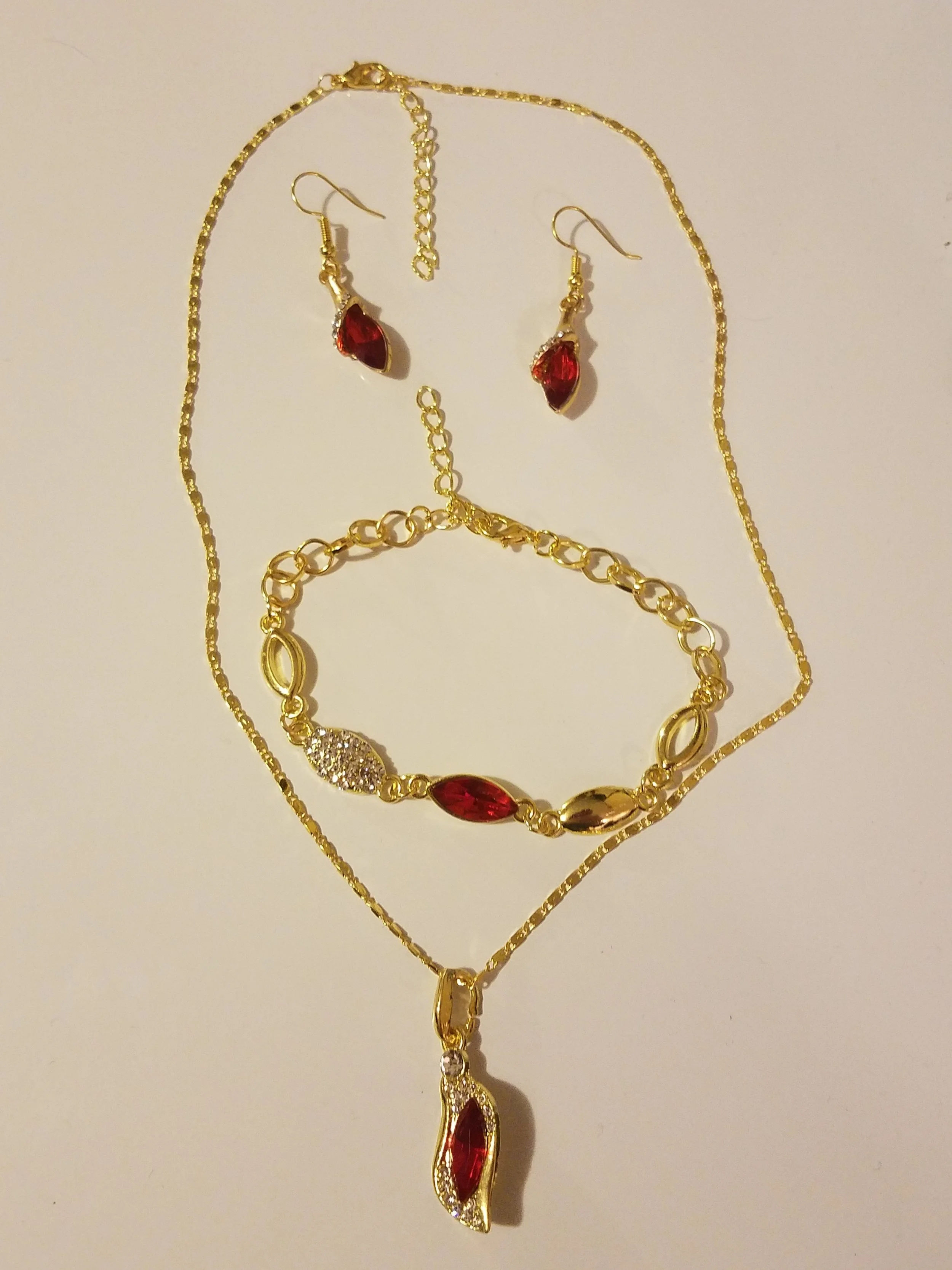 Gold jewelry set including a necklace, bracelet, and earrings with red and clear gemstones