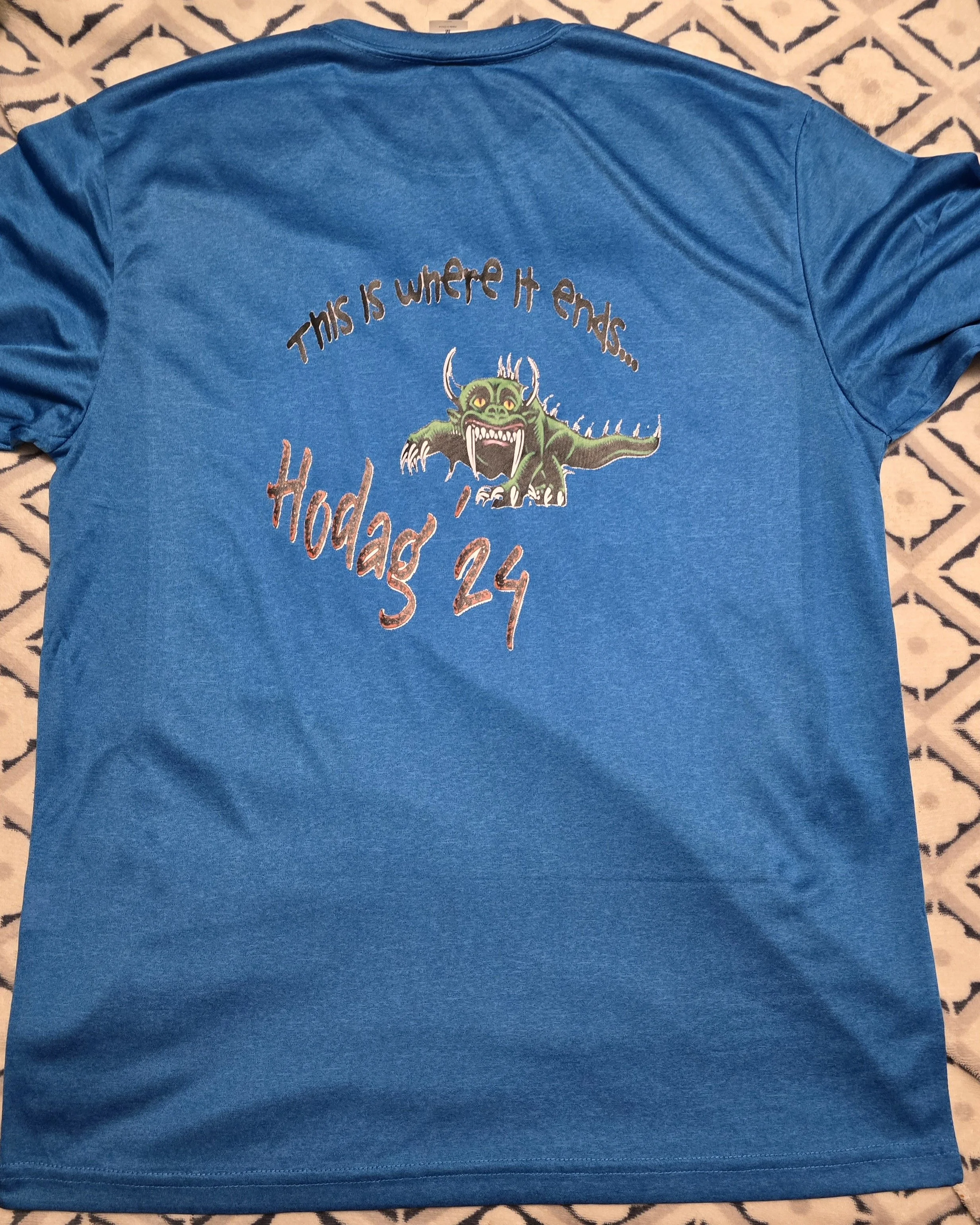 Blue T-shirt with an embroidered design of a green monster with horns and sharp teeth, accompanied by the text 'This is where it ends... Hodag 24'.