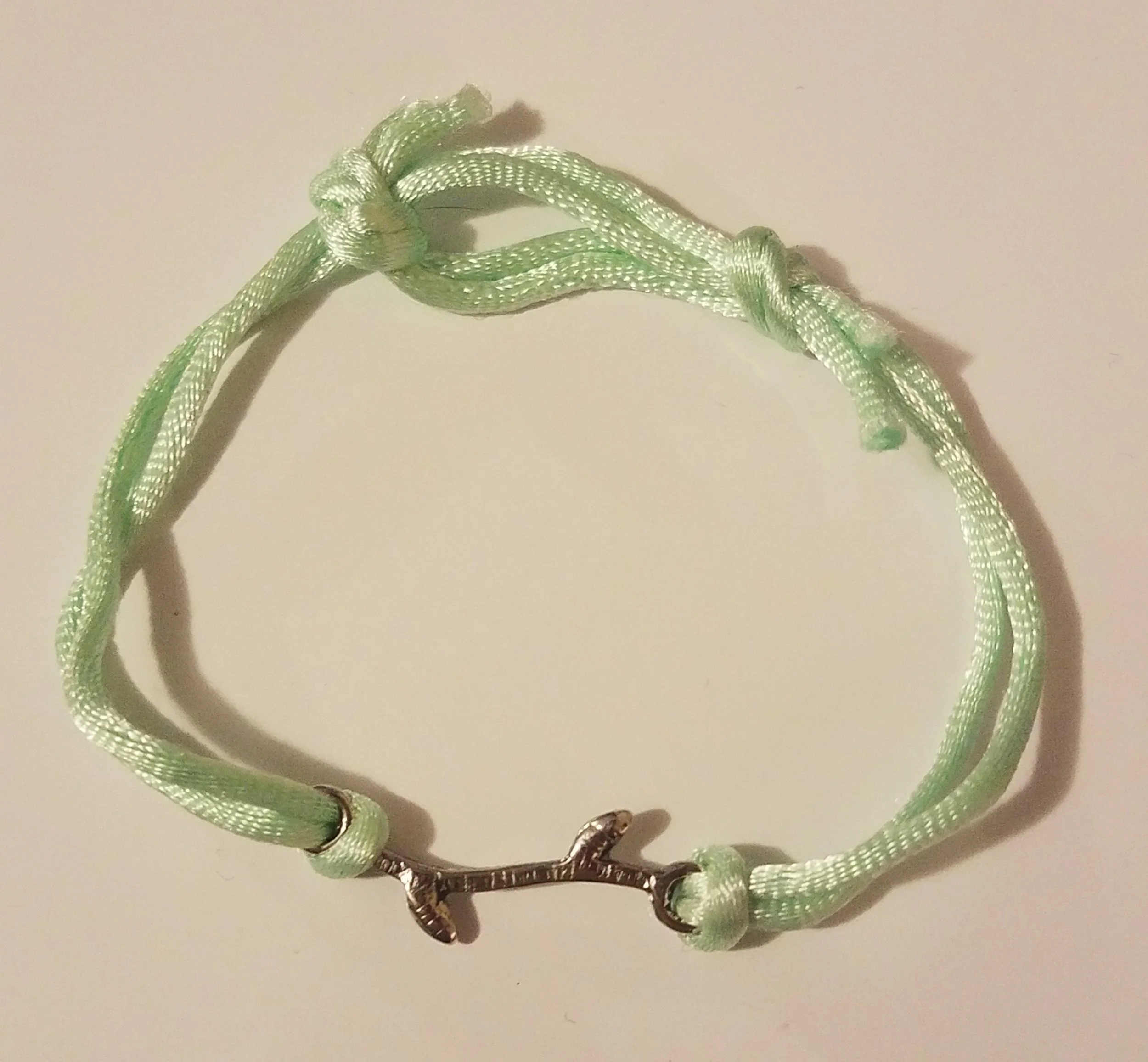 Light green cord bracelet with a silver anchor charm.