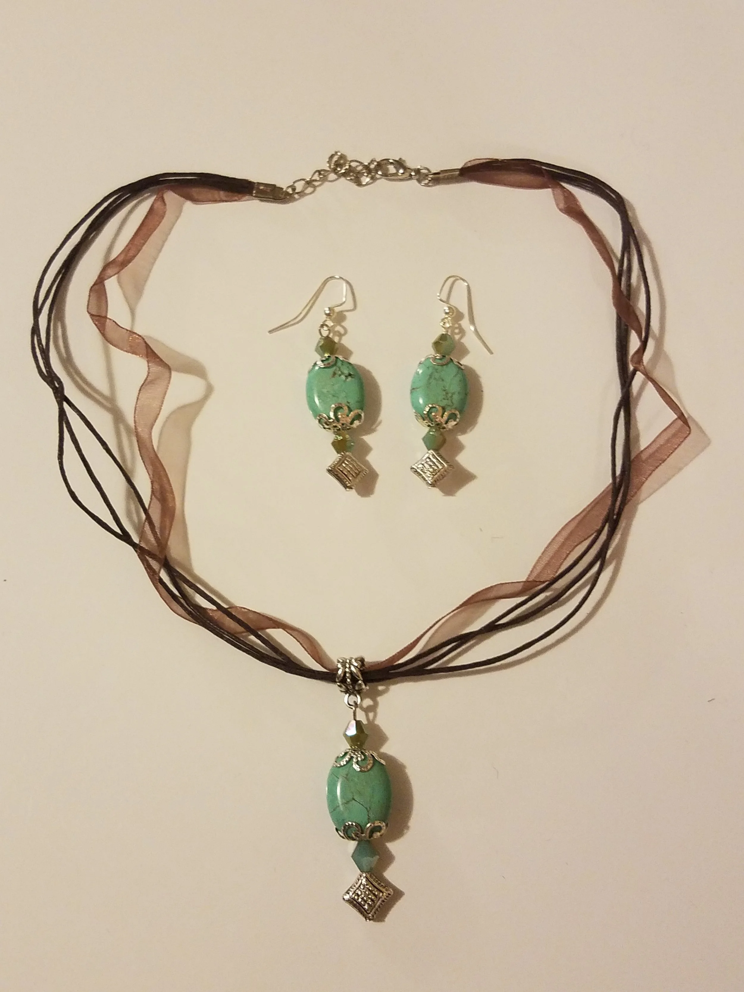 Set of turquoise jewelry including a necklace with a pendant and a pair of matching earrings on a white background.