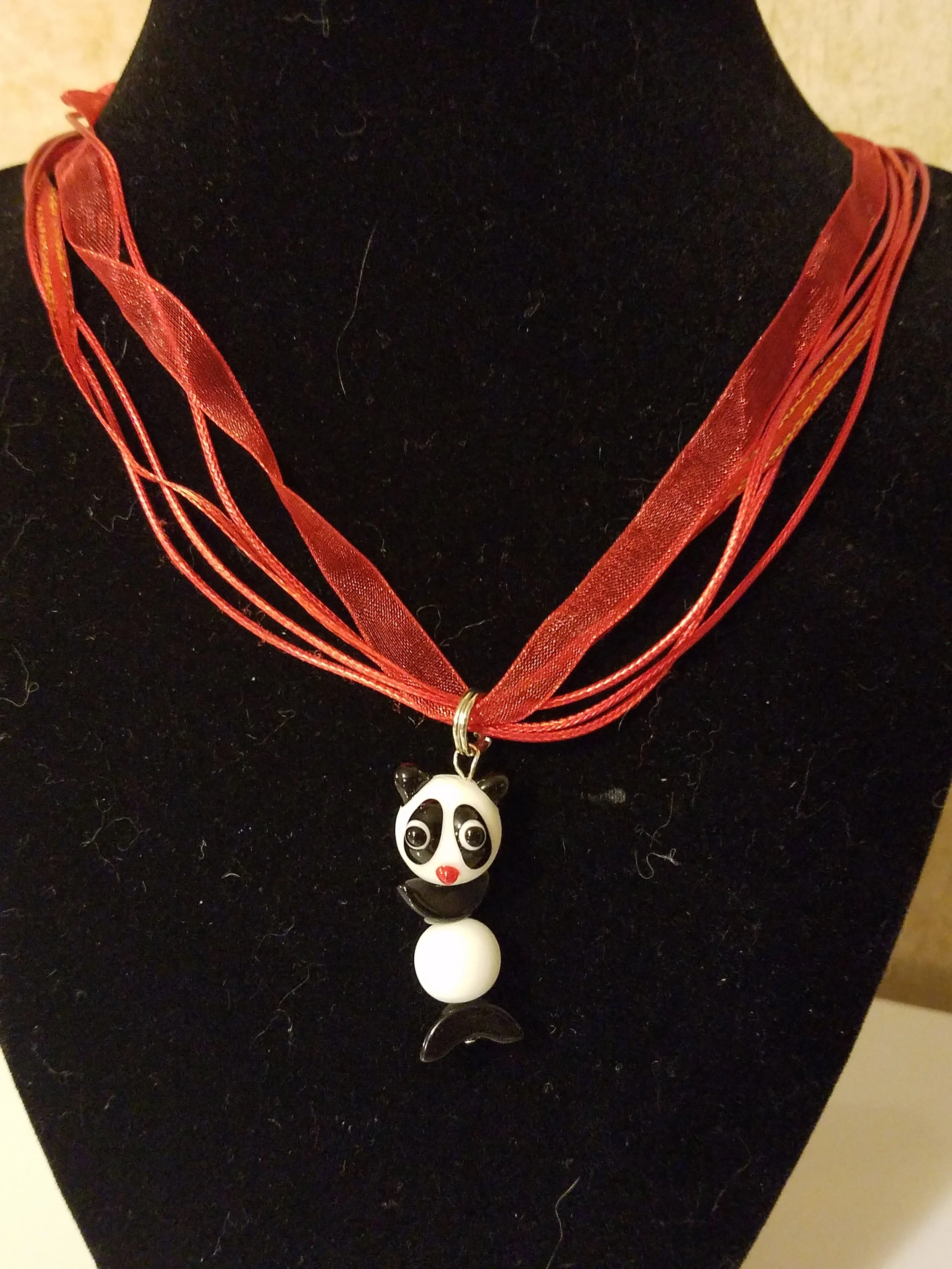 A necklace with a panda bear pendant on a black display stand.