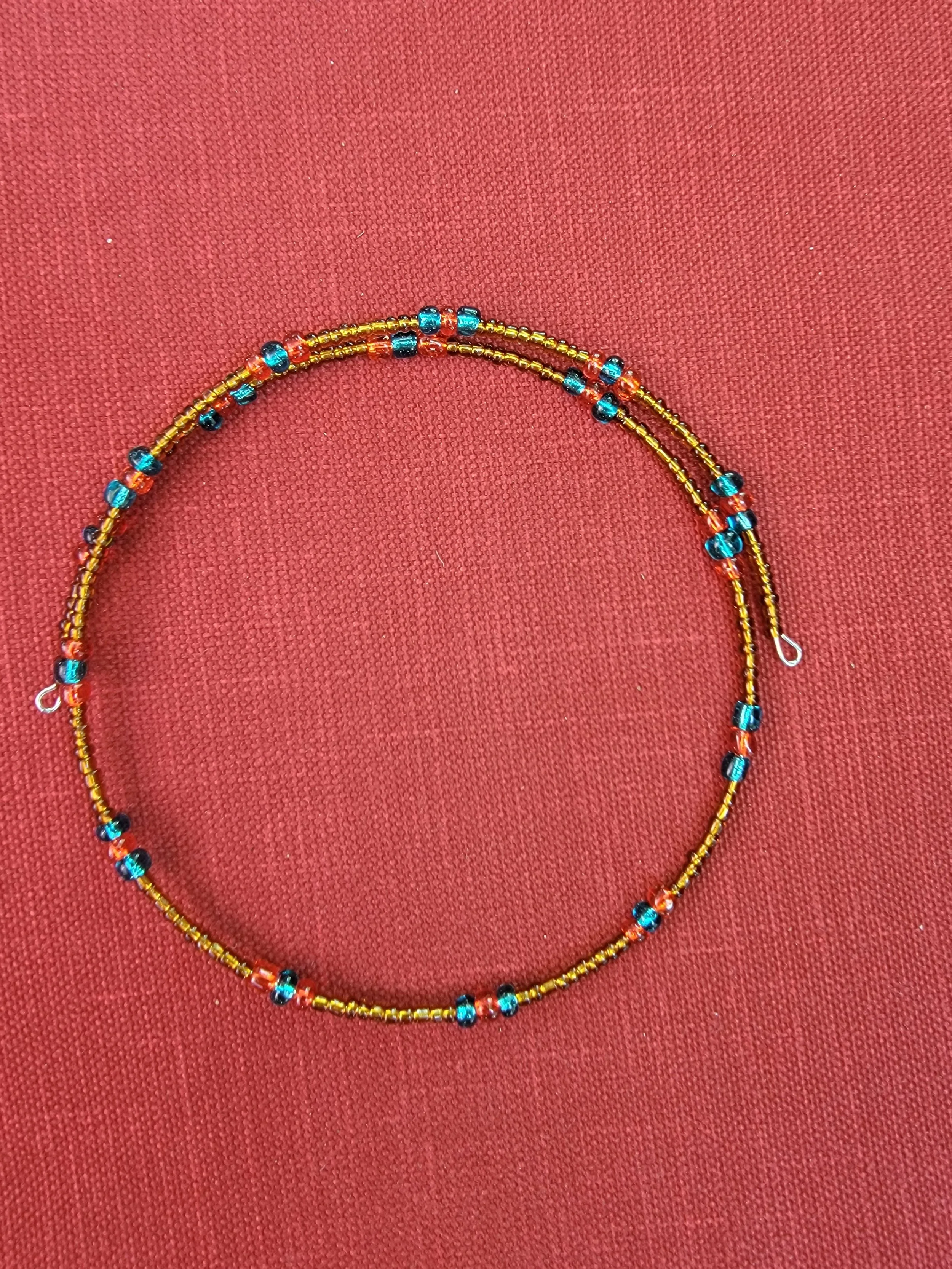 Colorful beaded necklace with small beads in blue, orange, and yellow, placed on a red fabric background.