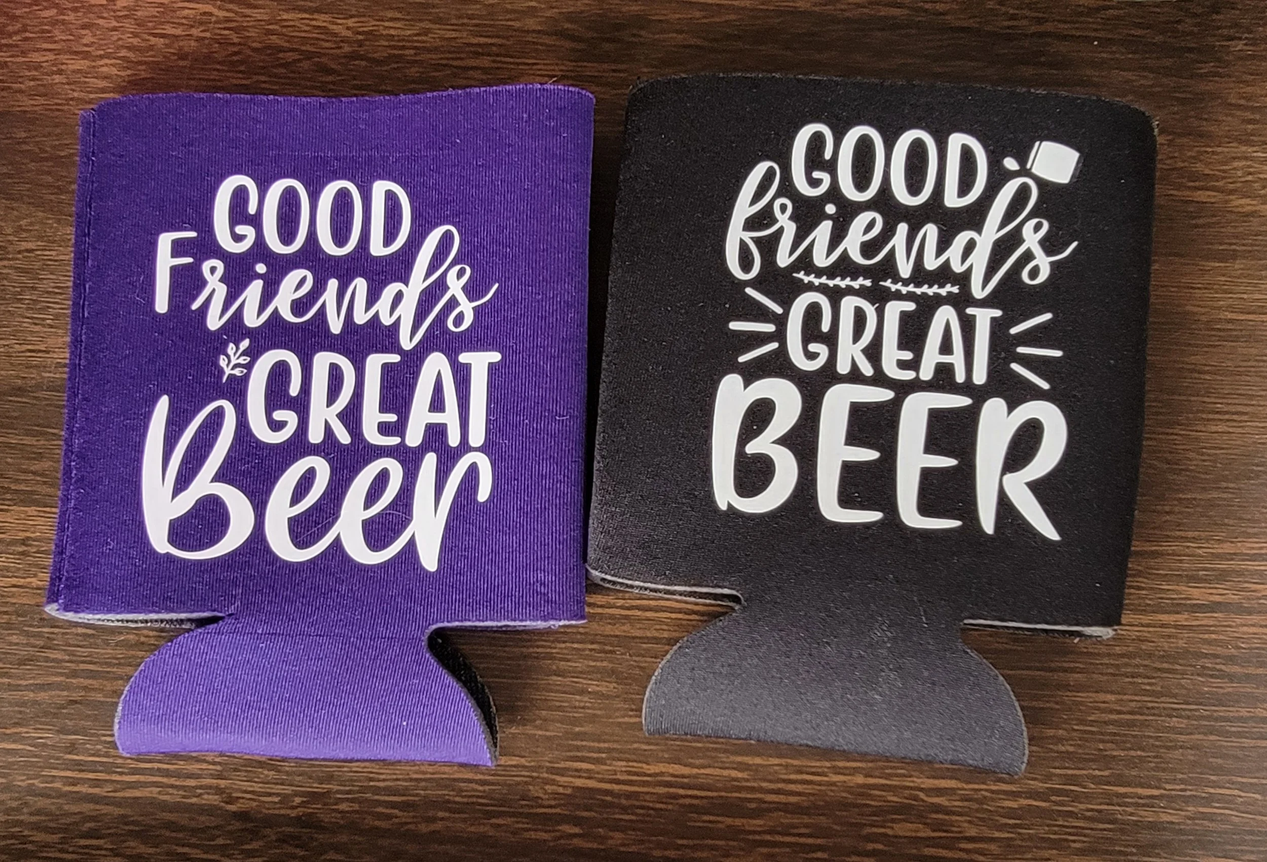 Set of two can cooler sleeves, one purple and one black, both with the phrase 'Good friends great beer' in white text.