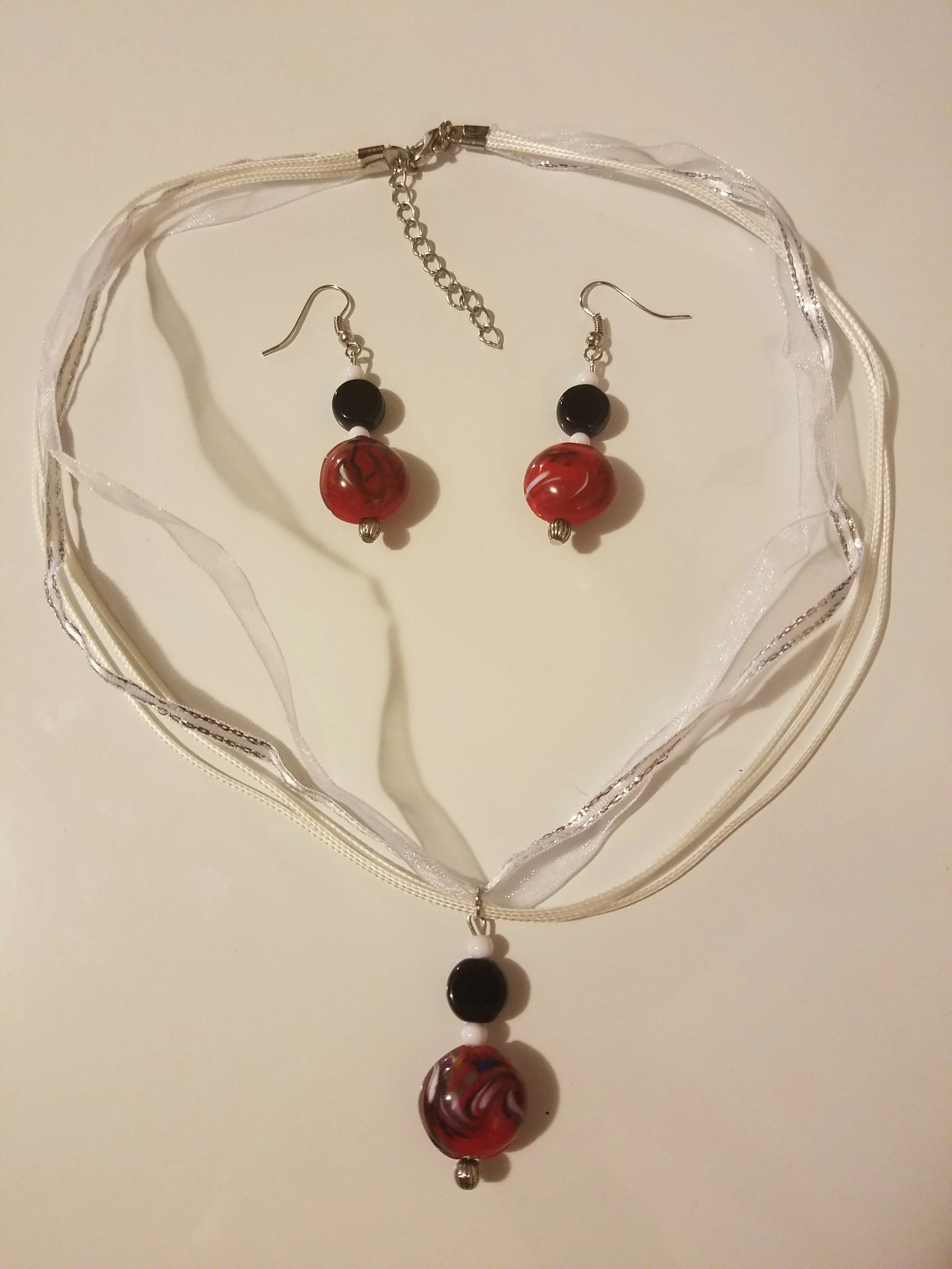 Set of jewelry including a necklace and matching earrings with large red and black marbled beads, displayed on a white surface