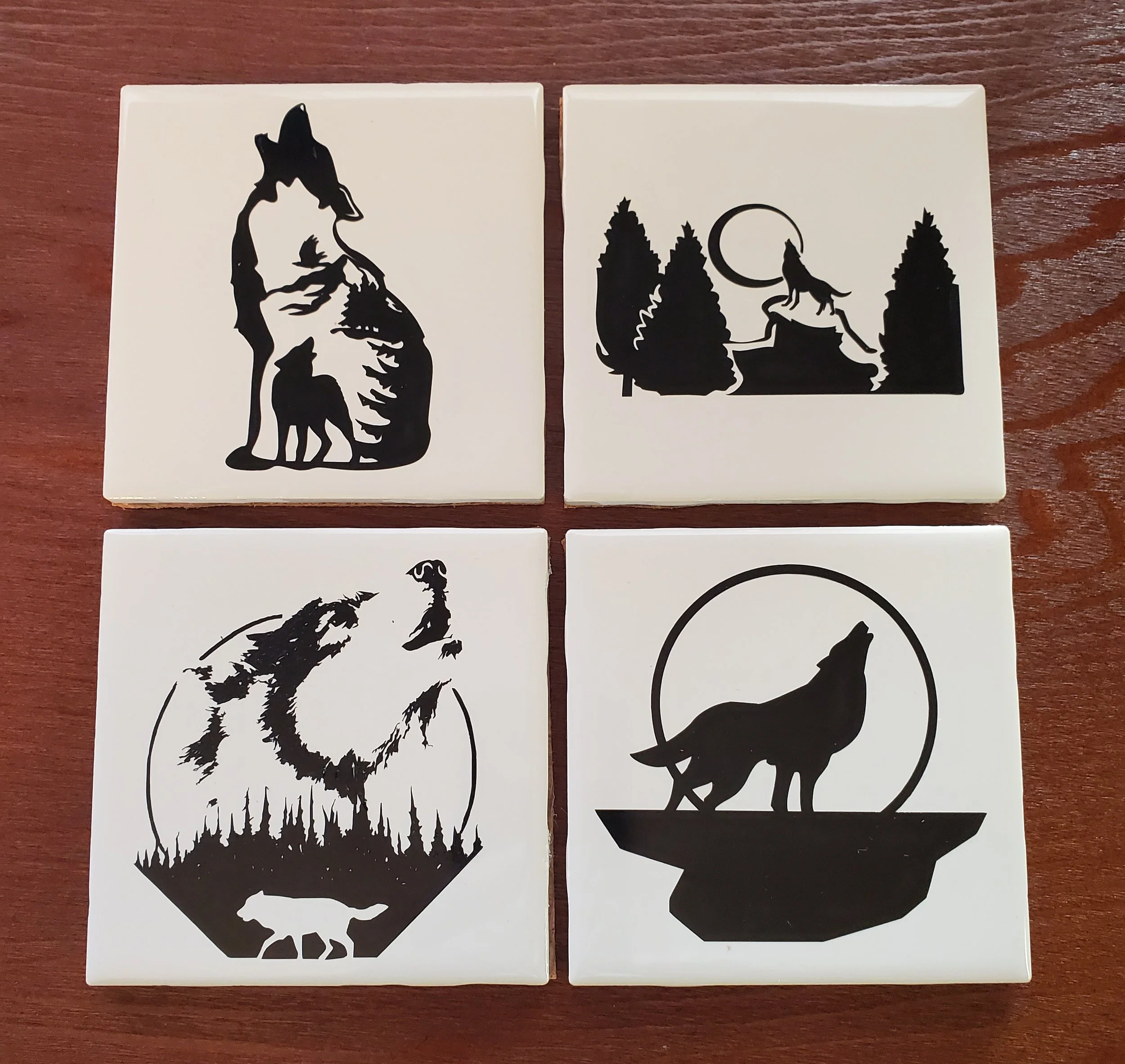 Set of four decorative tiles with black silhouette wolf-themed designs on white background, featuring wolves, trees, moon, and forest scenes.