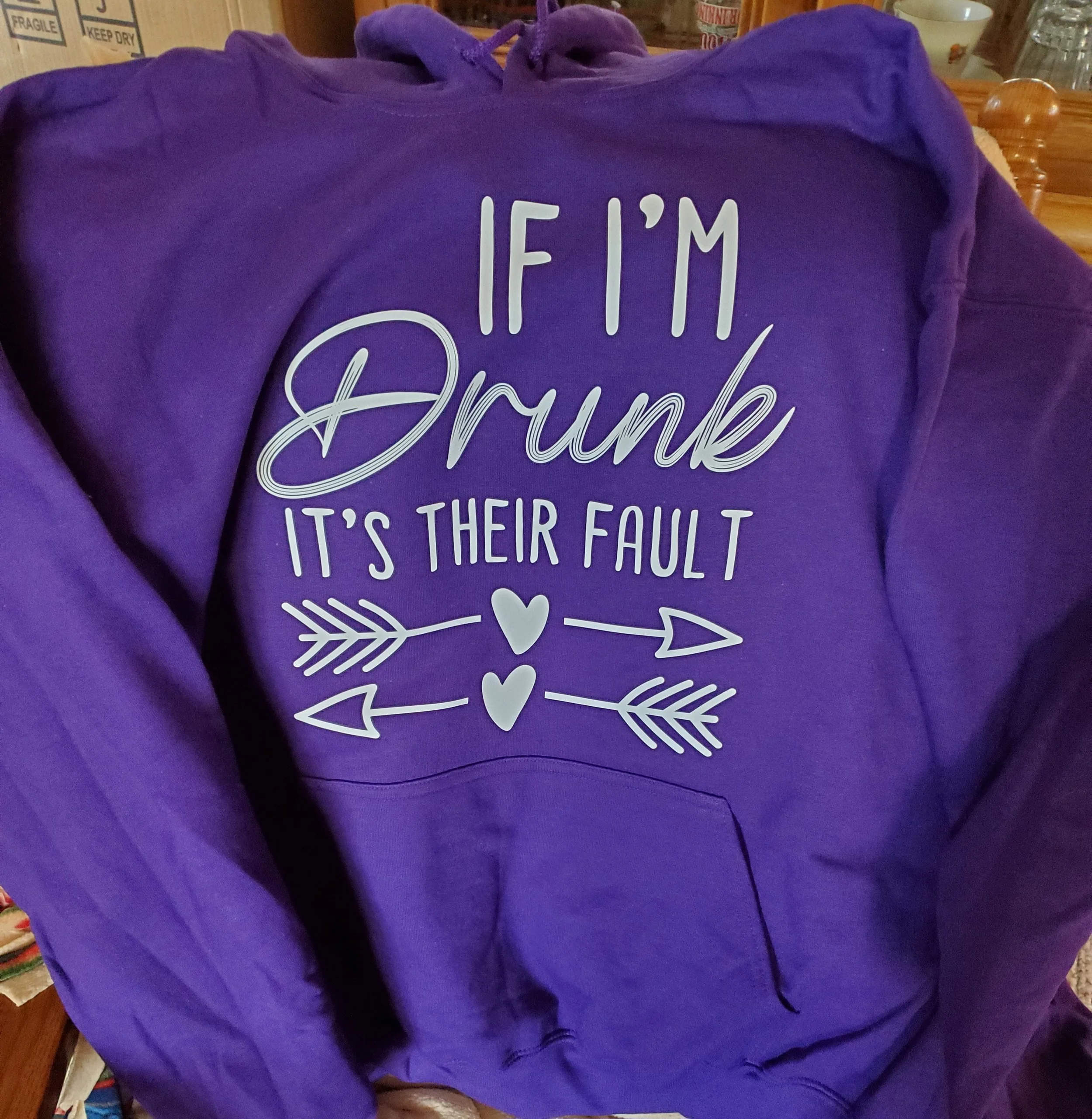 Purple hoodie with white text that reads, 'If I'm drunk, it's their fault,' decorated with two crossed arrows and three hearts.