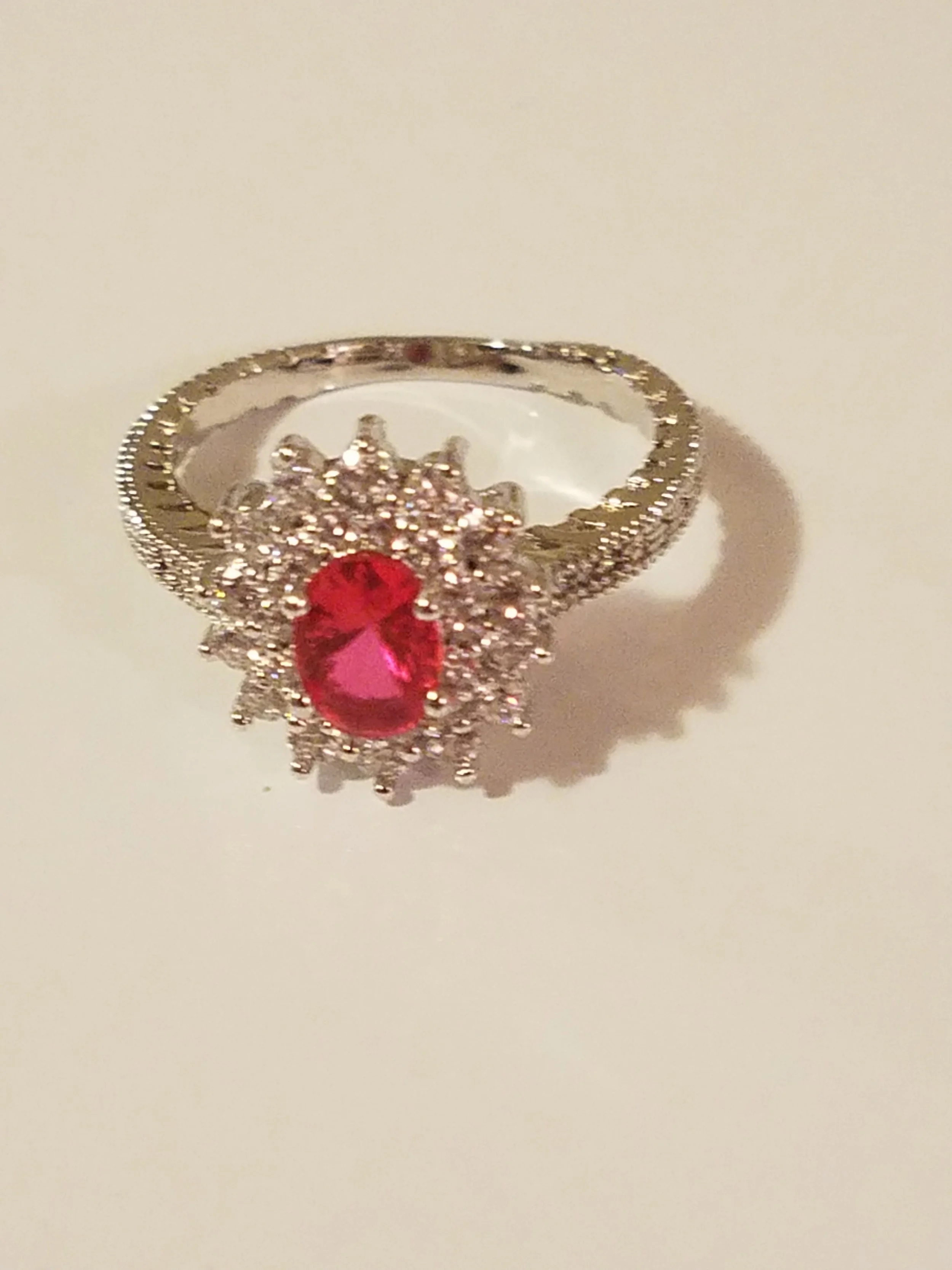 A silver ring with a pink gemstone surrounded by small clear stones.
