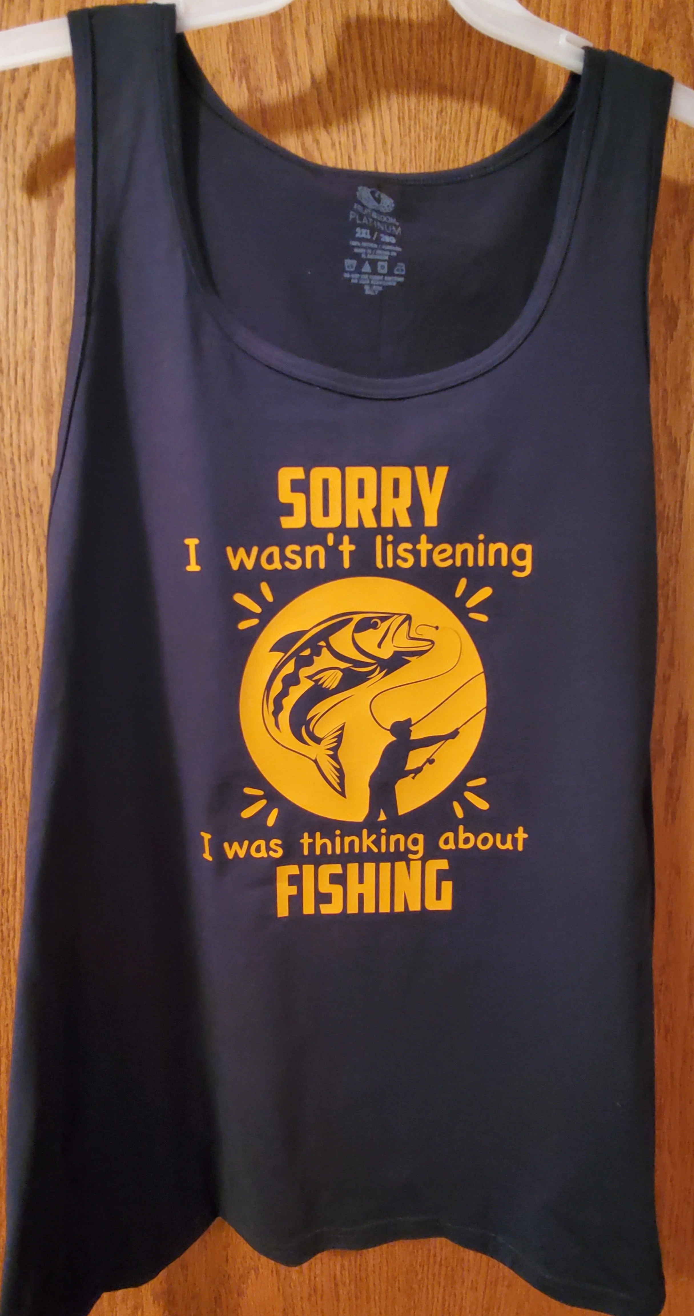 Black sleeveless T-shirt with yellow graphic and text that says, "Sorry I wasn't listening. I was thinking about fishing." featuring a fisherman and a large fish in a circle.