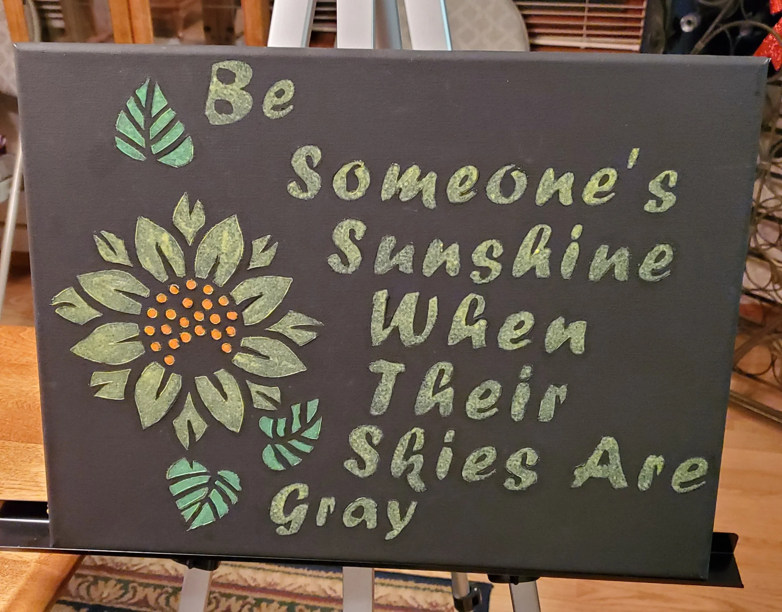 Decorative sign with a sunflower and leaves, displaying the quote: "Be someone's sunshine when their skies are gray."