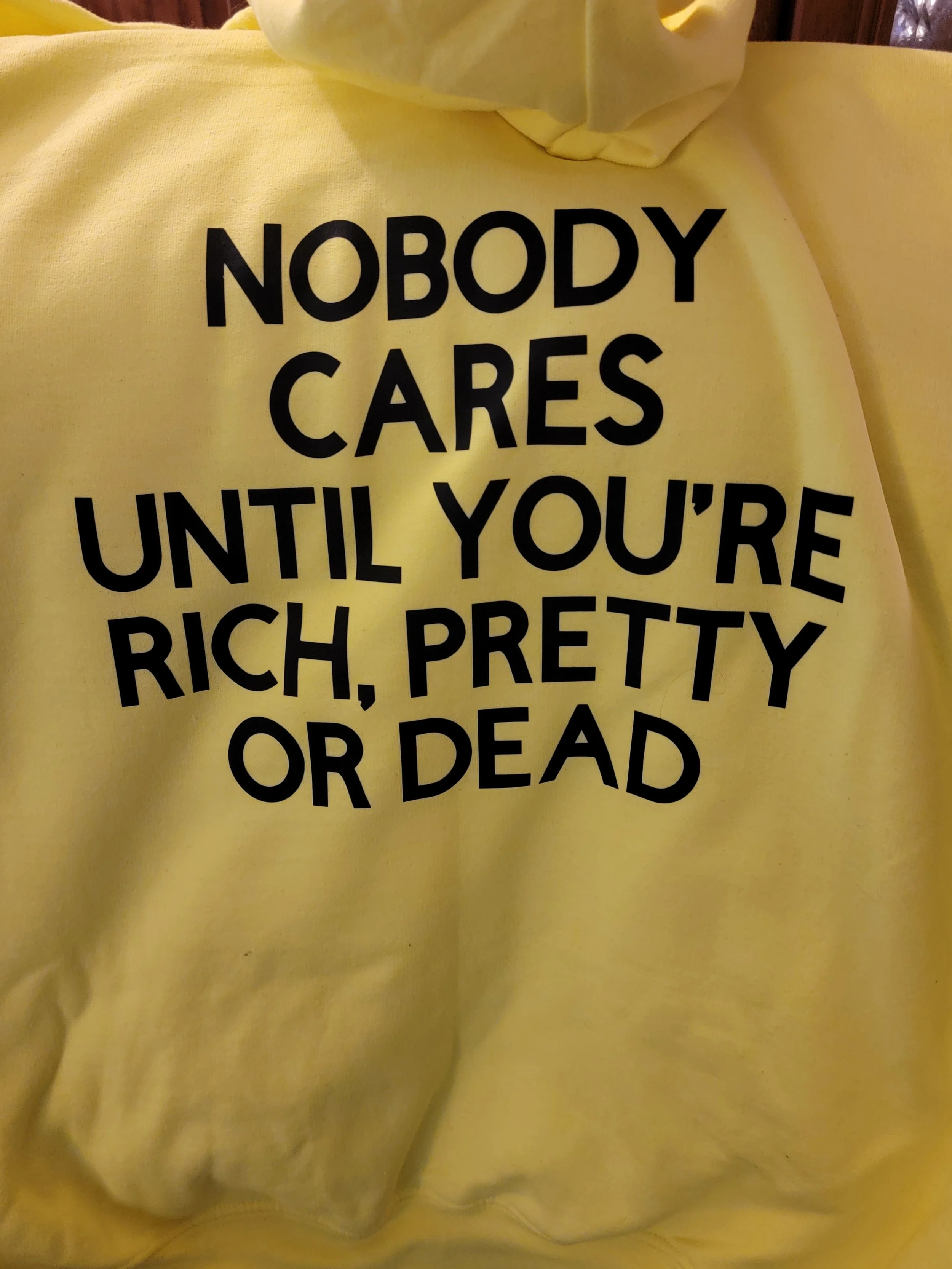 Yellow hoodie with black text that reads 'Nobody cares until you're rich, pretty or dead'.