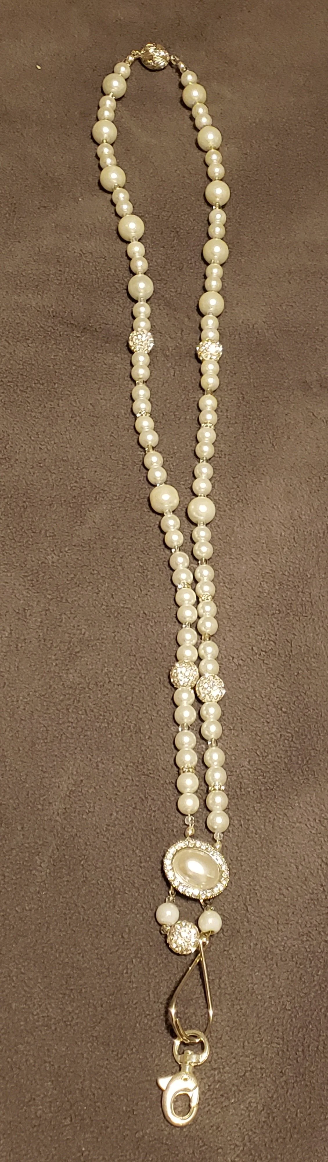 A pearl necklace with large pearl beads, sparkly decorative beads, and a large pearl pendant with rhinestones, attached to a safety pin clasp.
