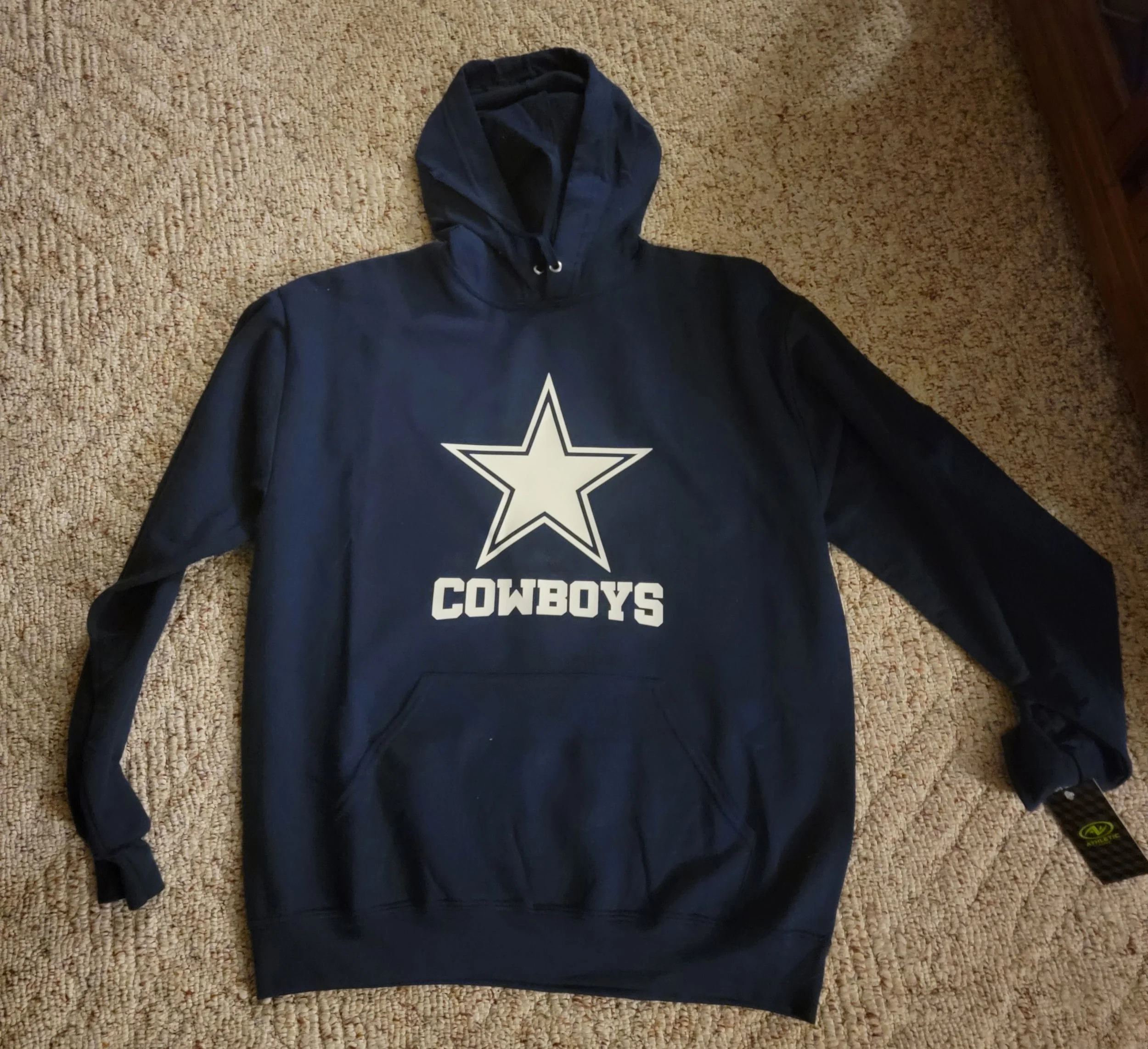 A navy blue hoodie with a large Dallas Cowboys logo and the word 'COWBOYS' printed on the front, lying on a beige carpet.
