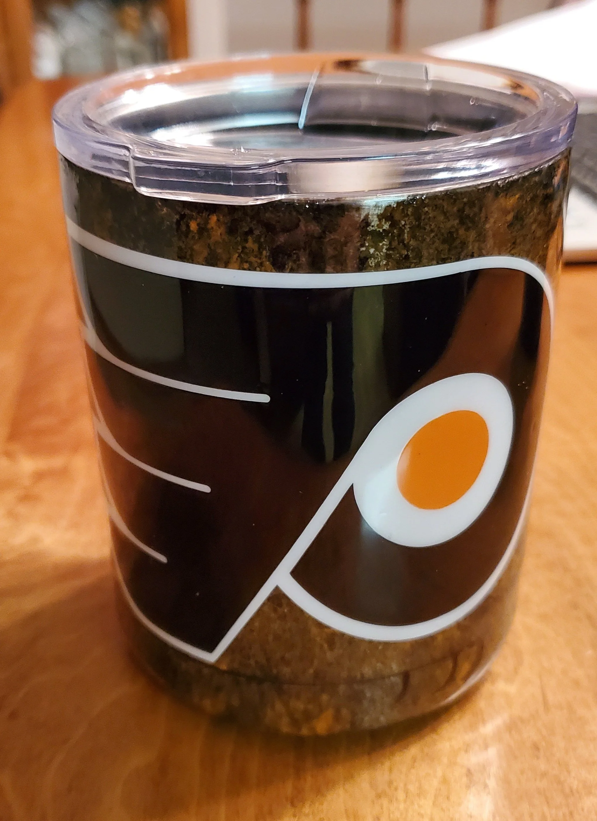 A jar of instant coffee with a black label, a white and orange logo, and a transparent plastic lid, sitting on a wooden surface.
