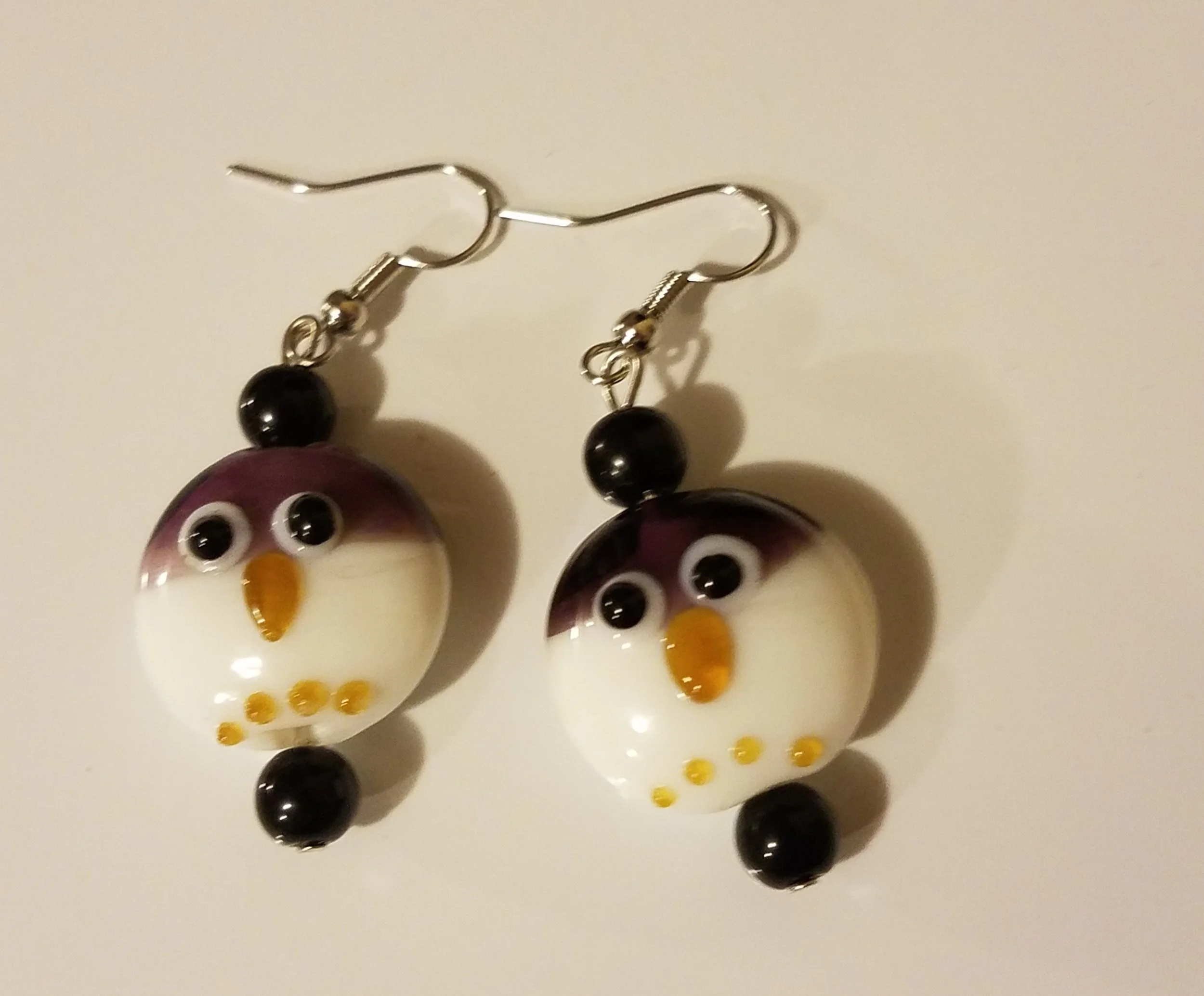 Penguin-shaped earrings with black, white, purple, and orange beads on a white background.