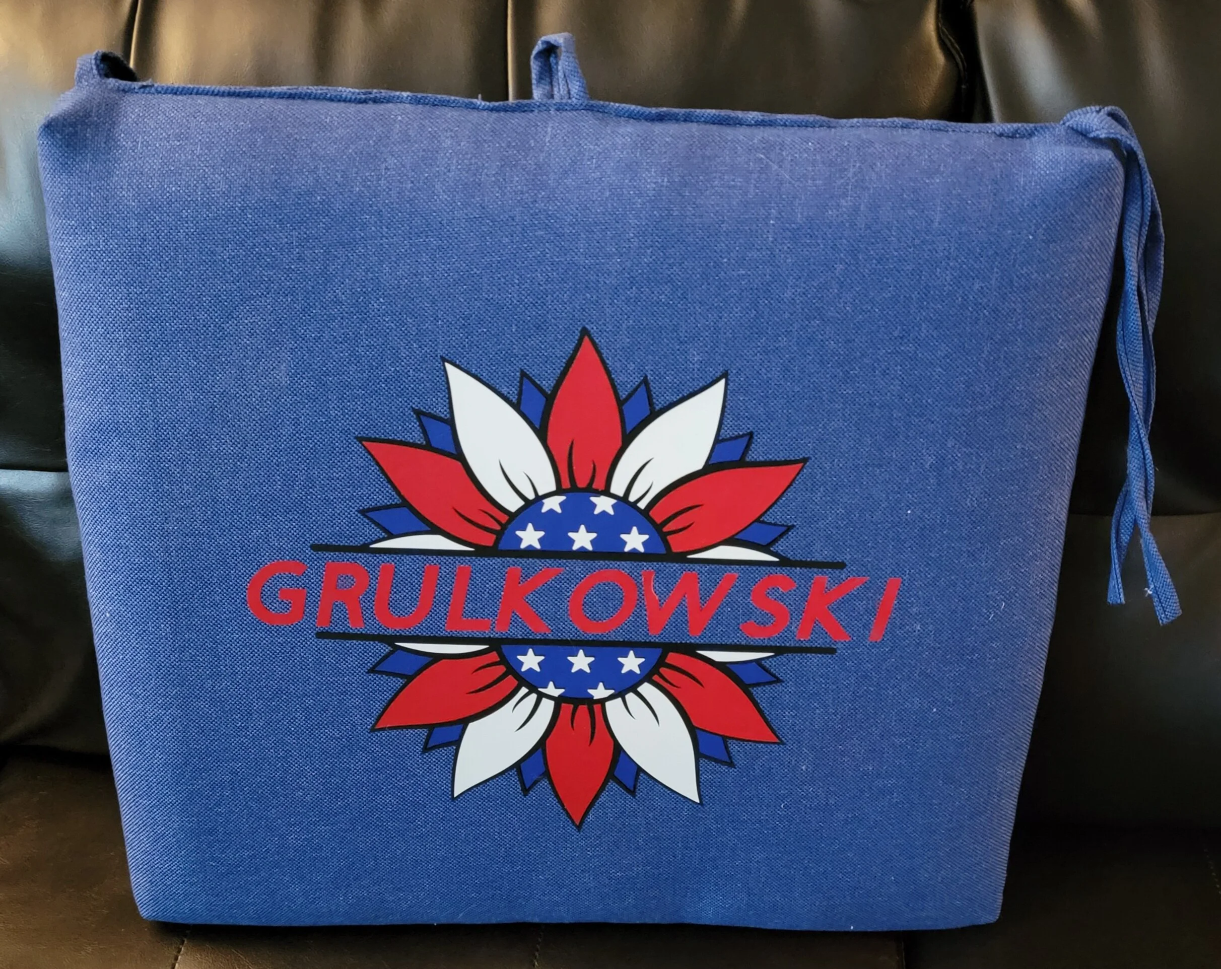 Blue fabric bag with a graphic design featuring a star-spangled circle surrounded by red, white, and blue petal-like shapes, and the word 'GRULKOWSKI' in red capital letters across the middle.