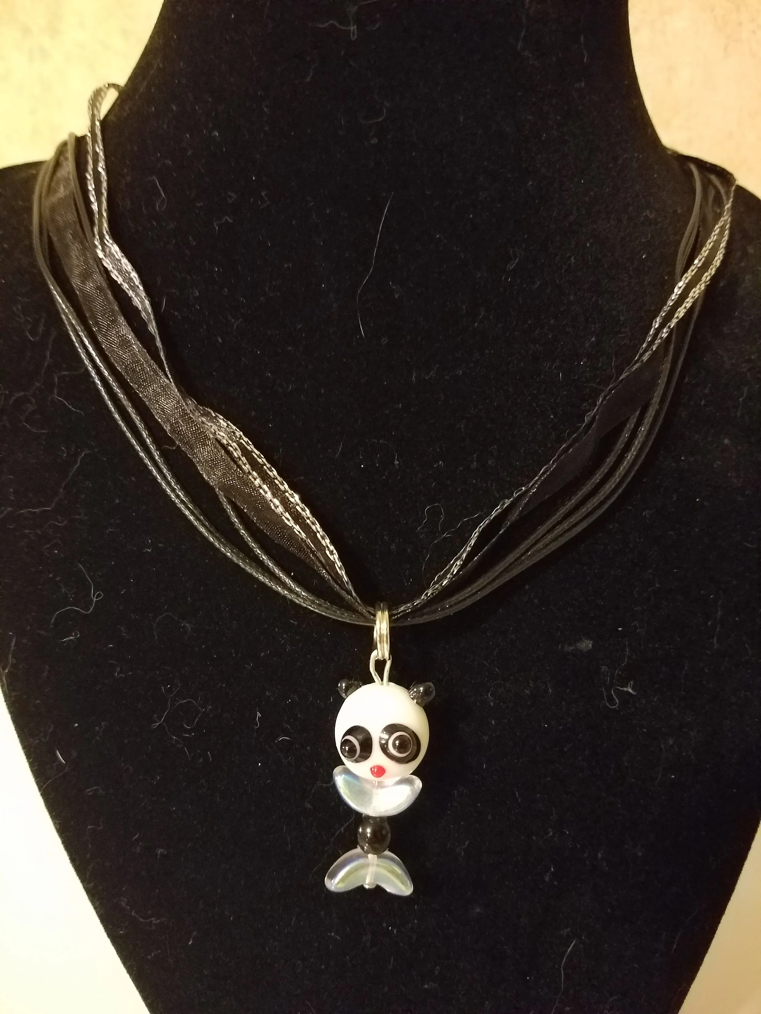 Black velvet display bust wearing a layered black necklace with a panda-shaped pendant.