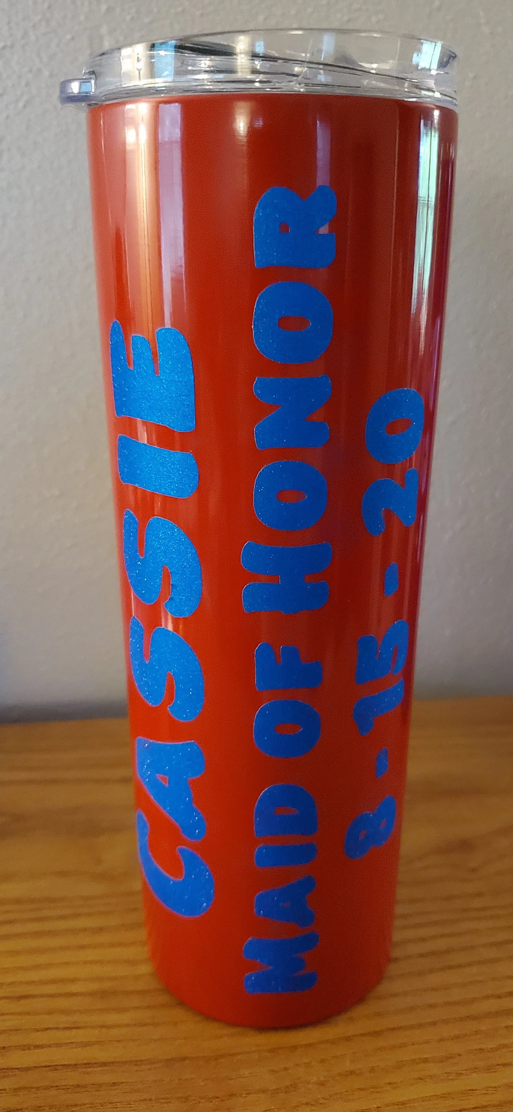 A red tumbler with blue text that reads 'CASSI' on the left side and 'HEDID FIONA 8-15-20' on the right side, placed on a wooden surface.