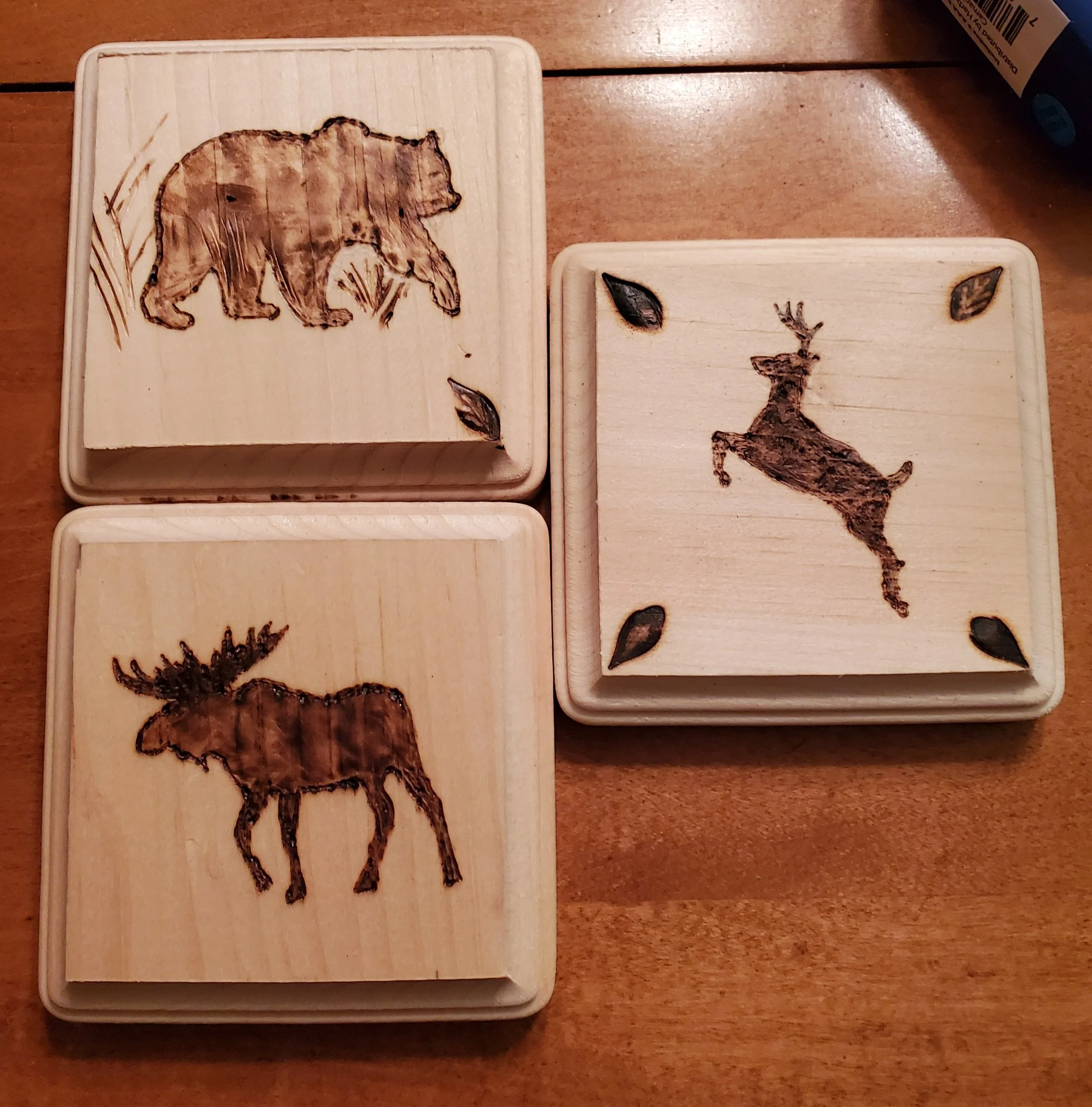 Set of three wooden coasters with engraved wildlife images: a bear, a deer, and a moose.