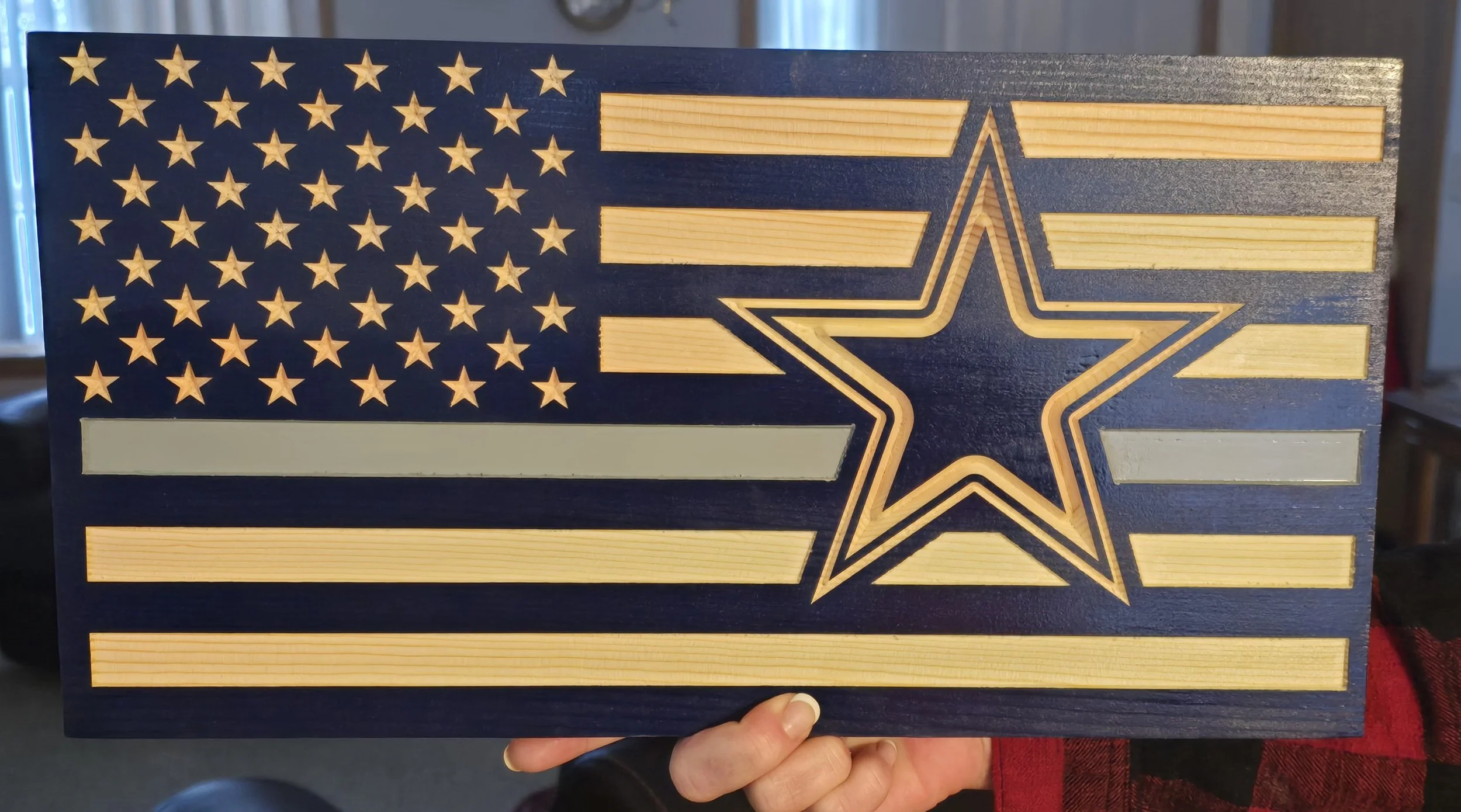 A wooden American flag wall art with a star and stripe design, featuring a large star outline in the center and rows of stars and stripes painted in blue and gold.