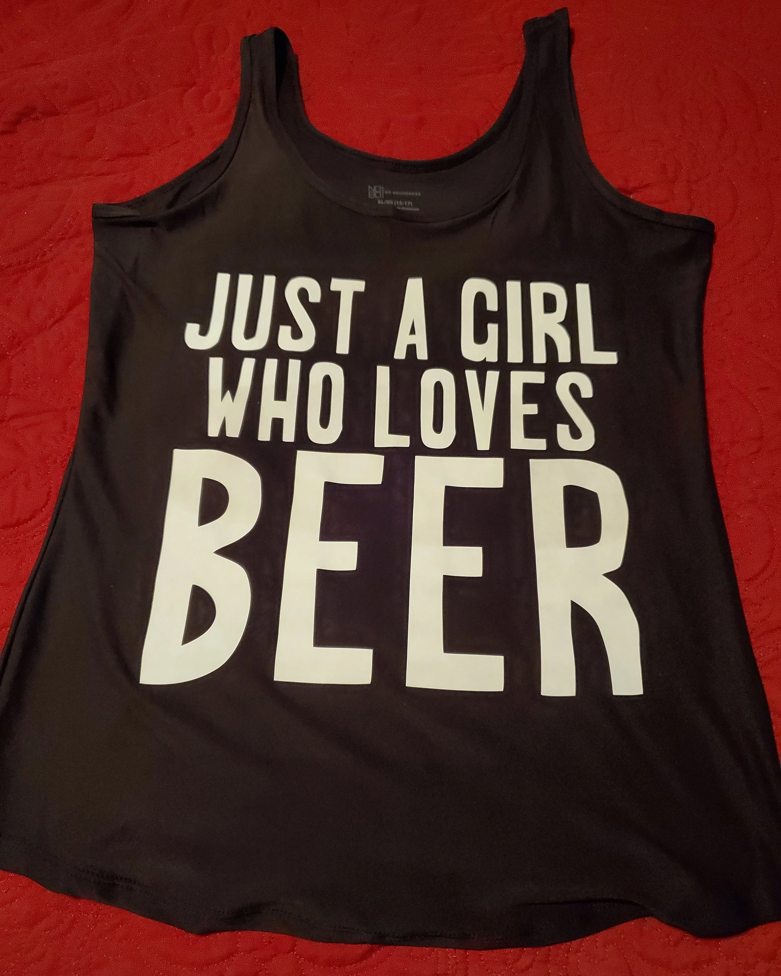 Black tank top with white text that reads 'JUST A GIRL WHO LOVES BEER' displayed on a red surface.