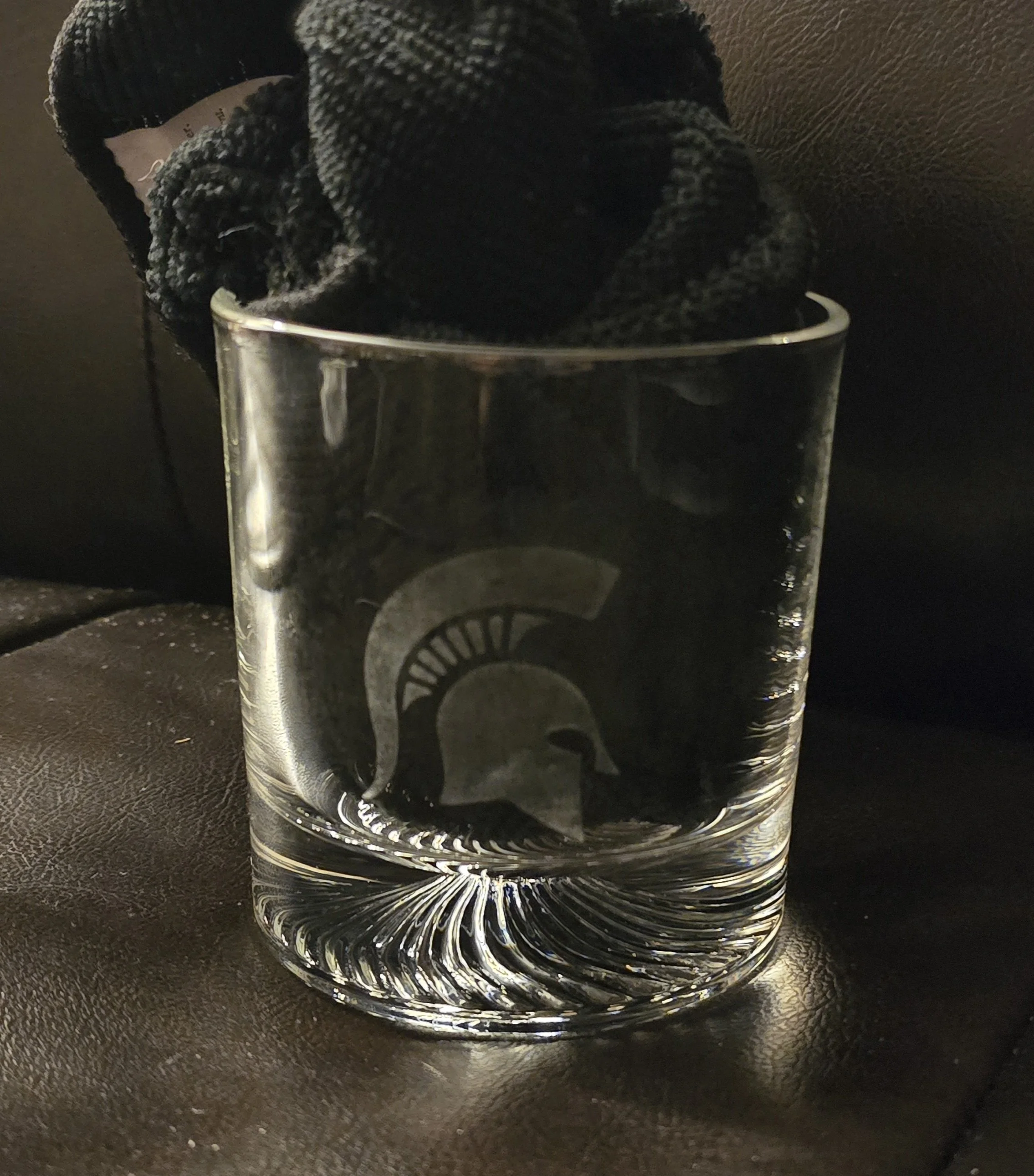 A clear glass filled with water and a black cloth, with the Michigan State Spartans logo etched on the glass.
