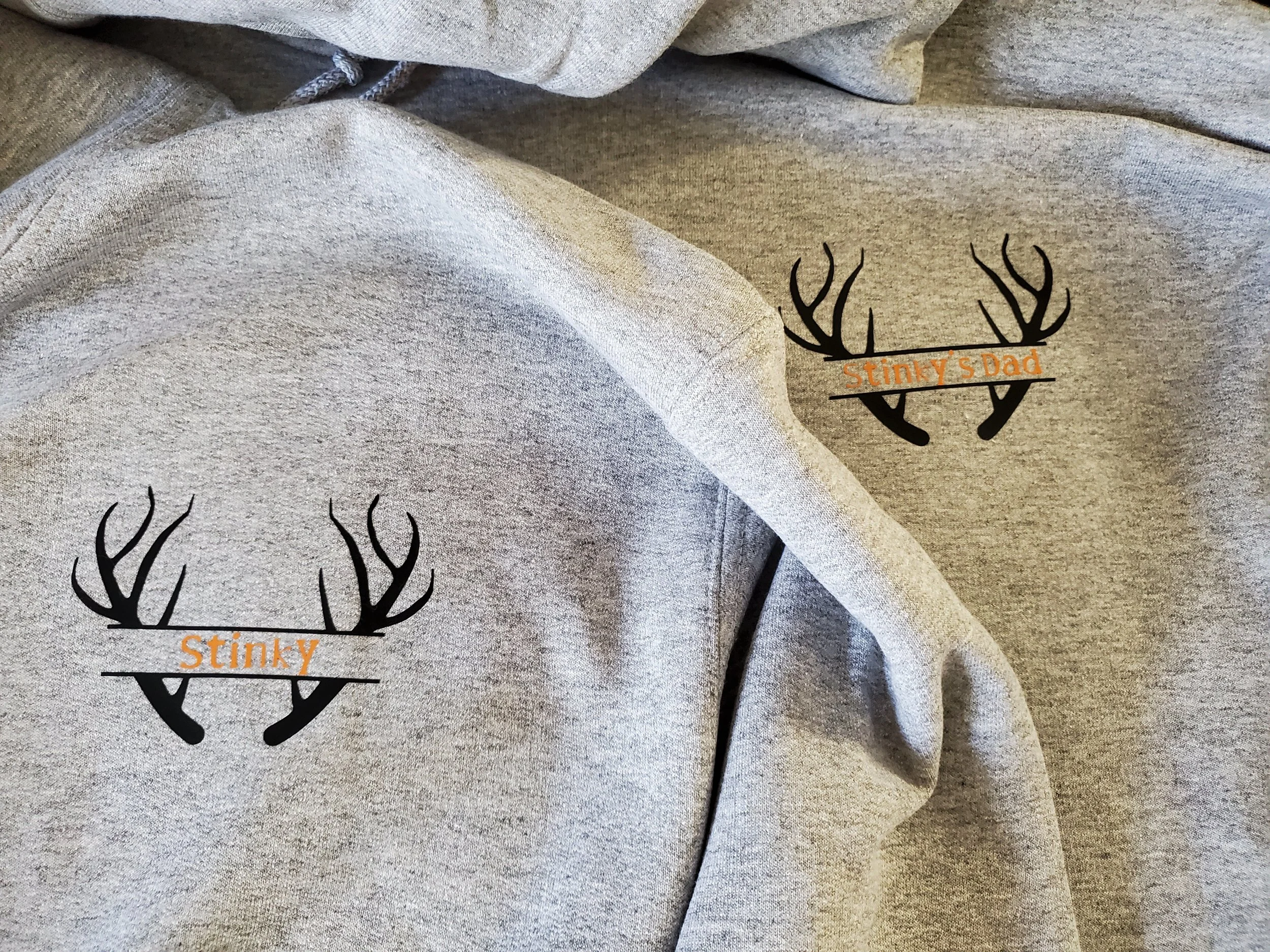 Gray hoodie with a black and orange logo of antlers and the text 'Stinky' and 'Stinky's Dad' printed on it.