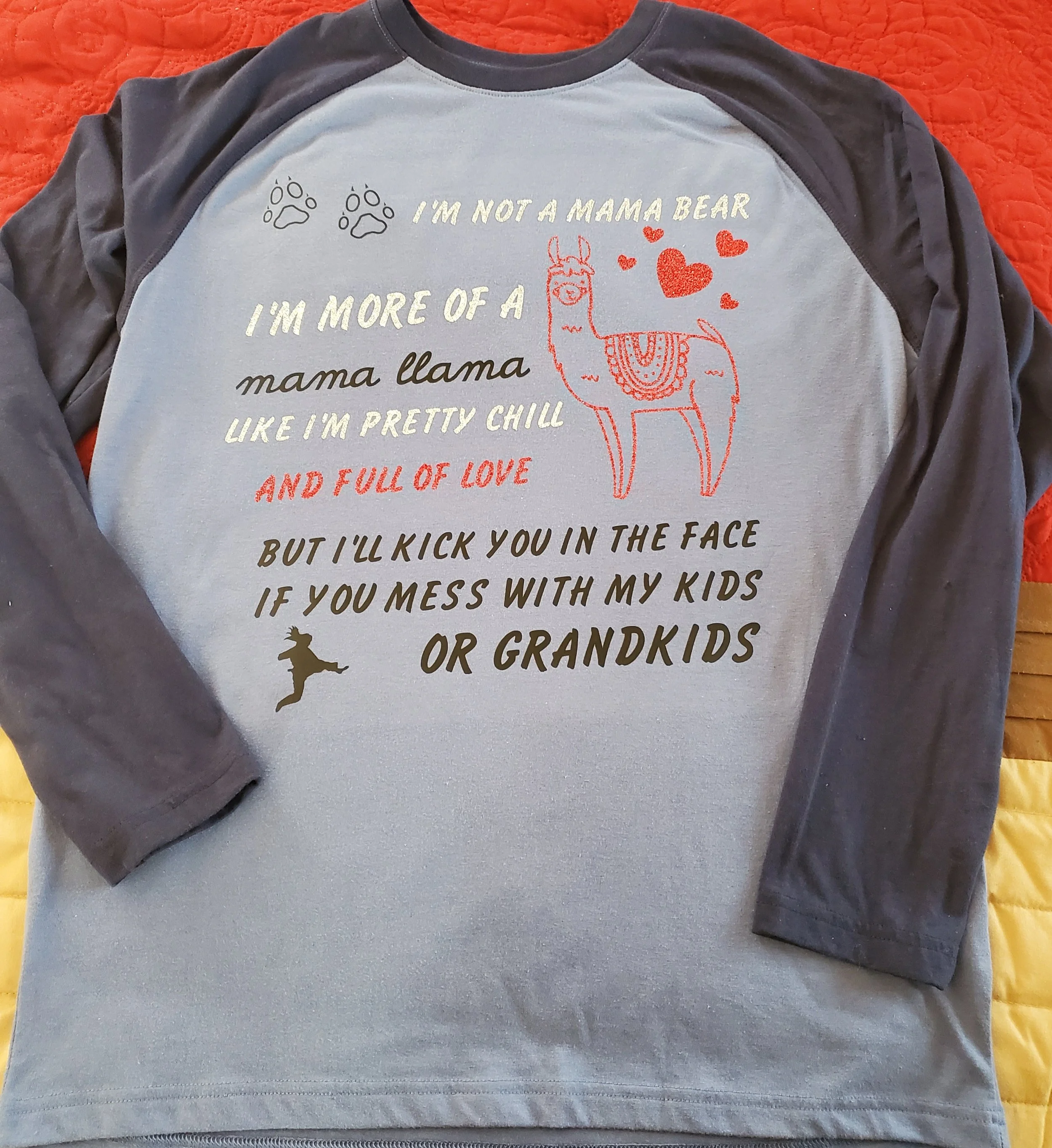 Long-sleeve shirt with a humorous message about motherhood, featuring paw prints, a llama illustration, hearts, and a small figure of a person jumping.