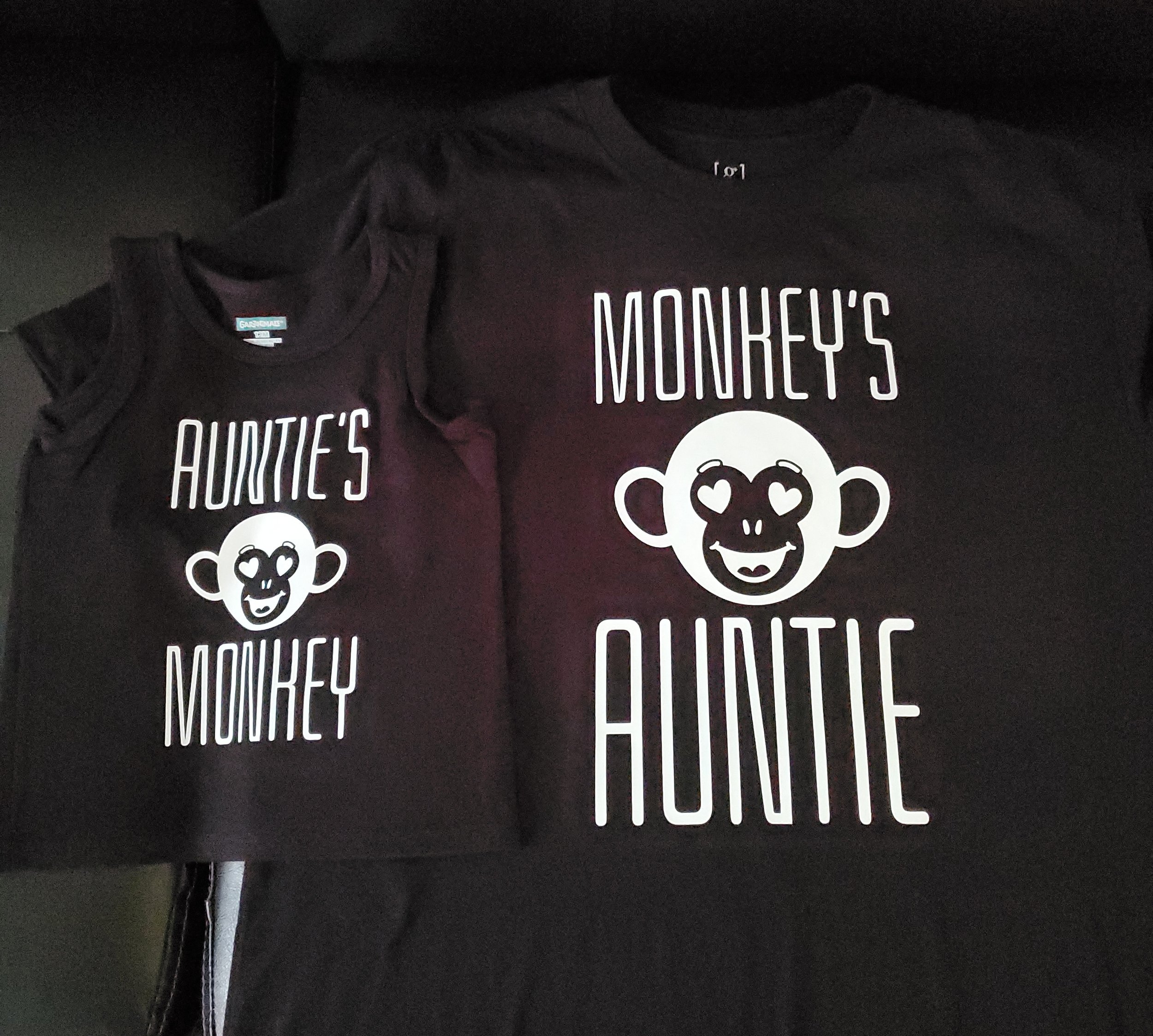 Black T-shirts with a white cartoon monkey face and text 'Auntie's Monkeys'.