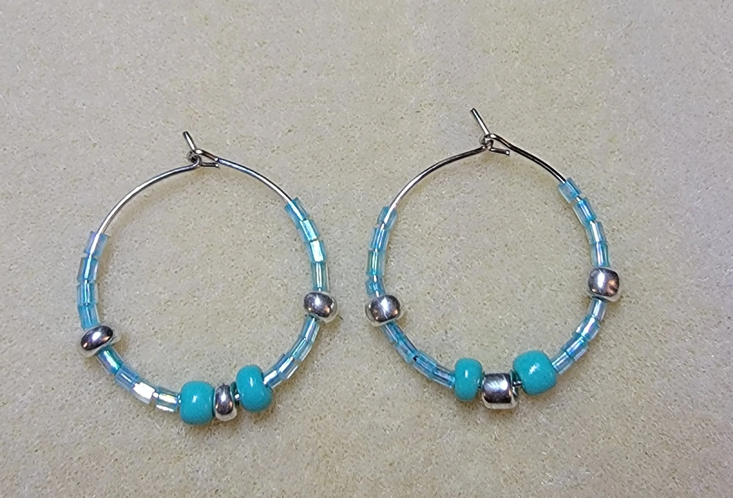 A pair of hoop earrings made with small blue and silver beads on a light beige surface.