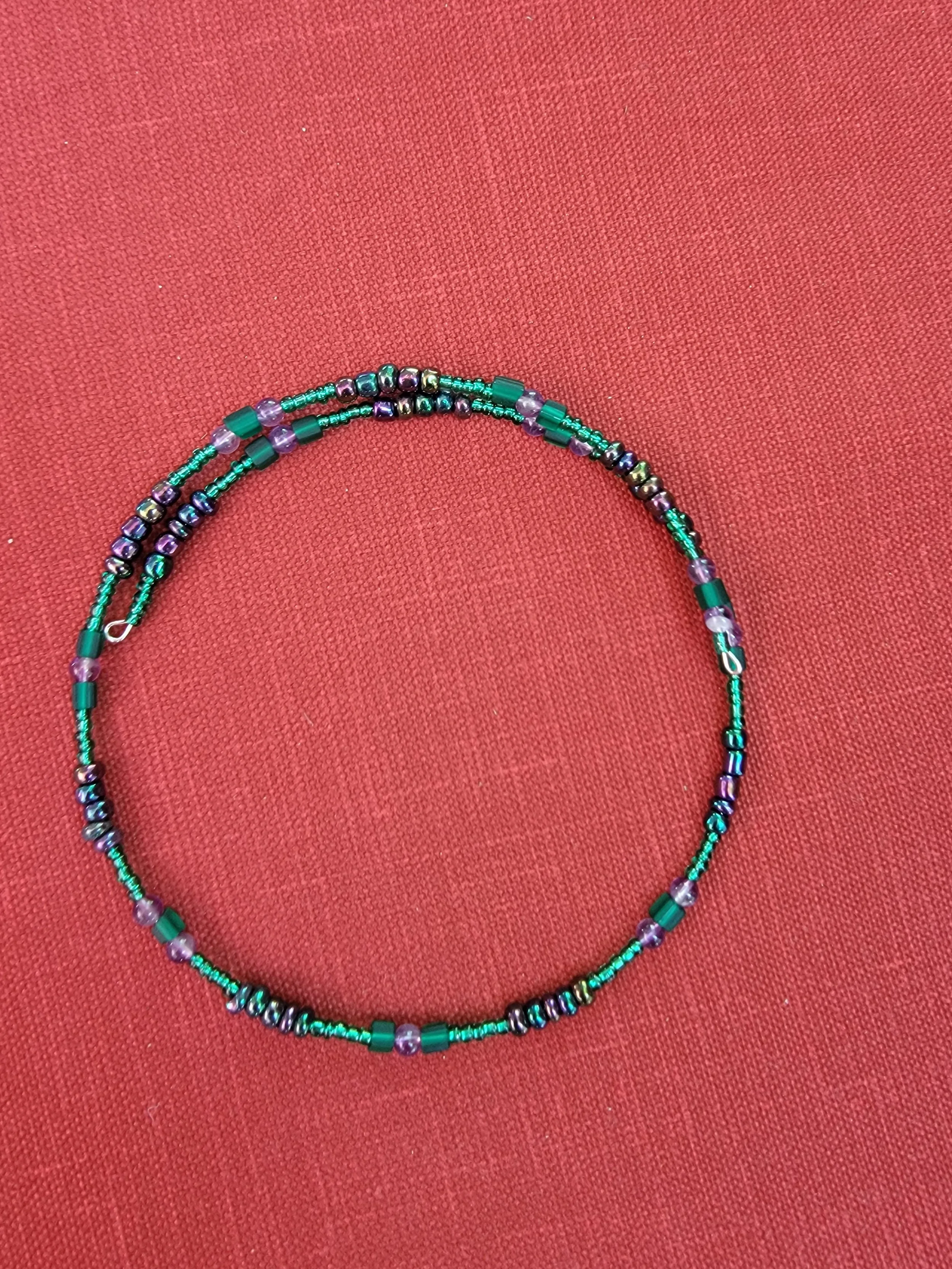 A beaded necklace with green, purple, and multicolored beads on a red fabric background.