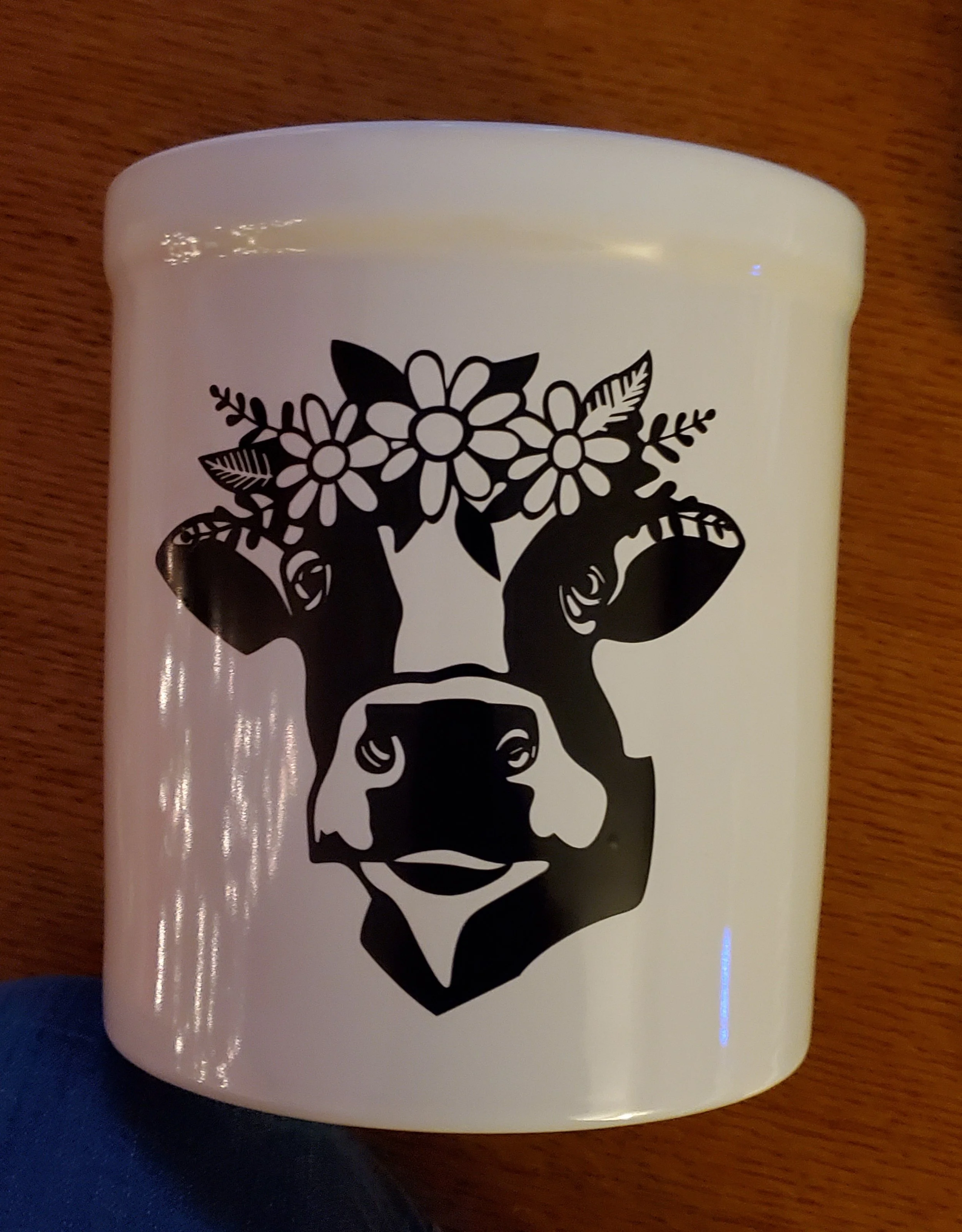 A white container with a black graphic of a cow's head with flowers and leaves on top.