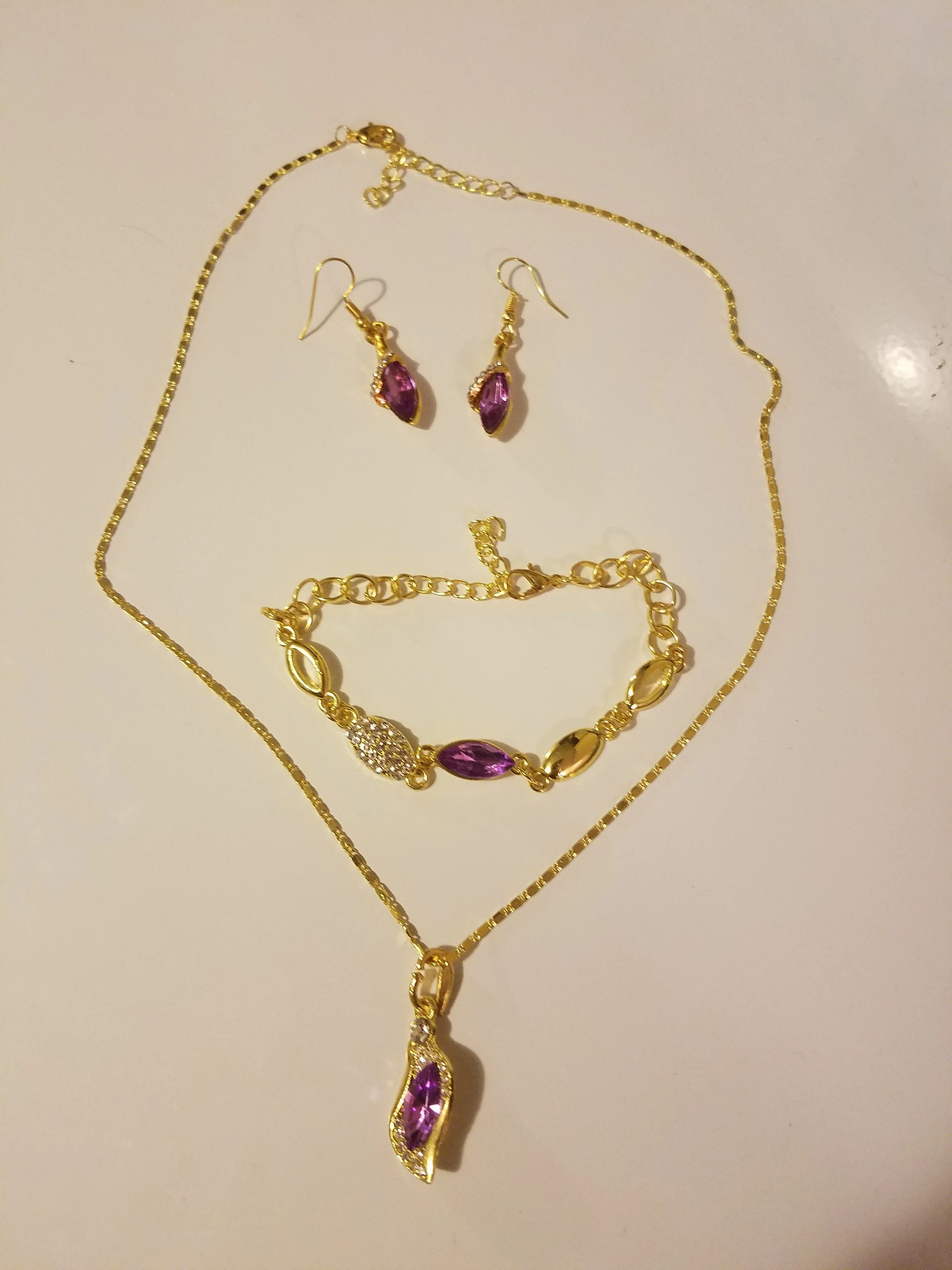Gold jewelry set with purple gemstones, including a necklace, earrings, and a bracelet, arranged on a white surface.