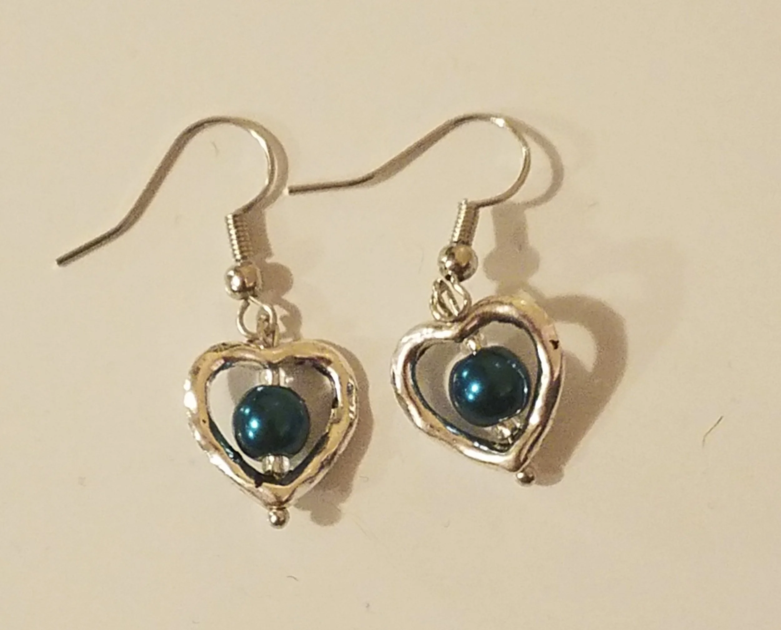 Silver heart-shaped drop earrings with a black spherical bead in the center.