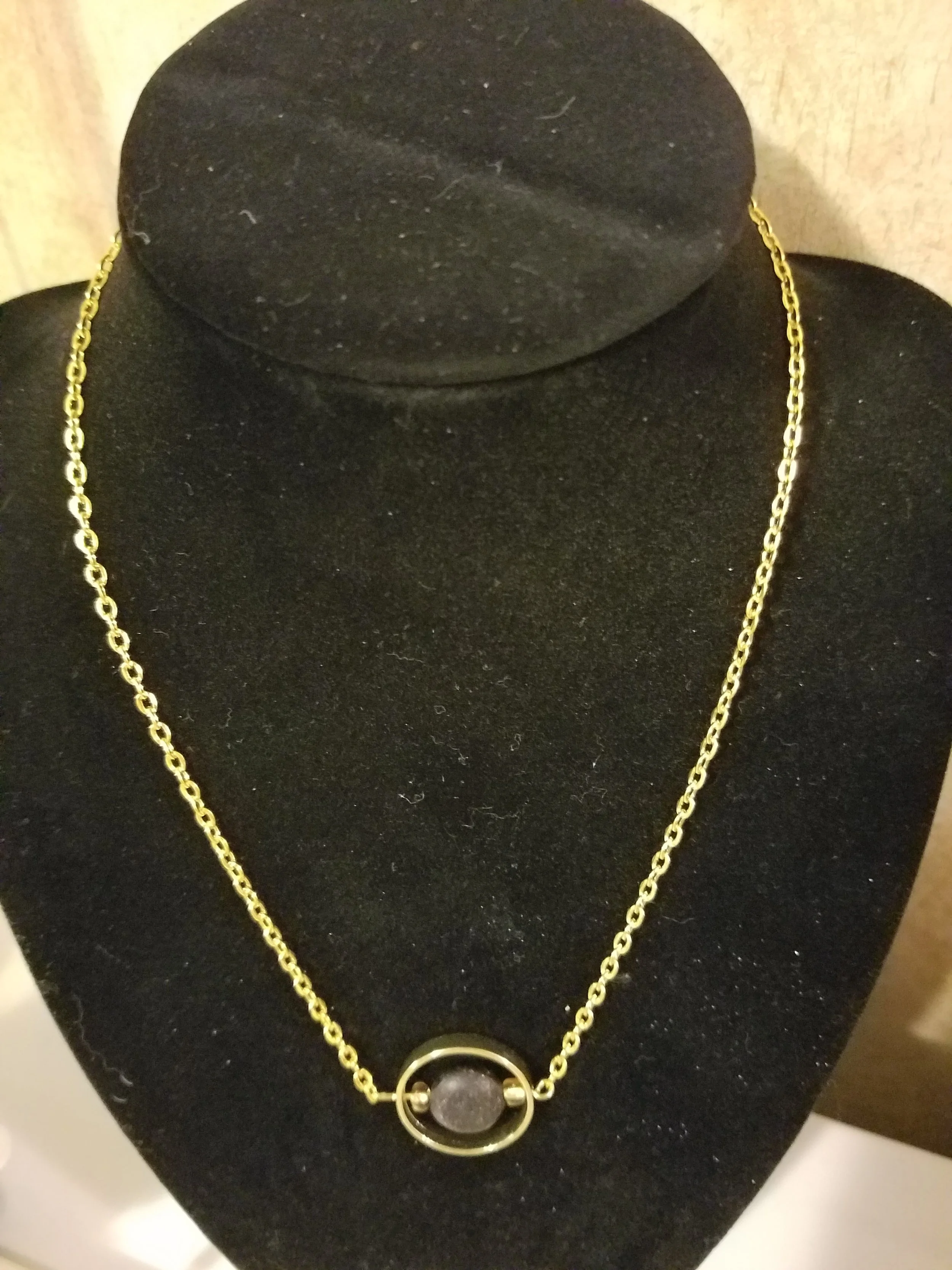 Gold necklace with a circular pendant displayed on a black jewelry stand.