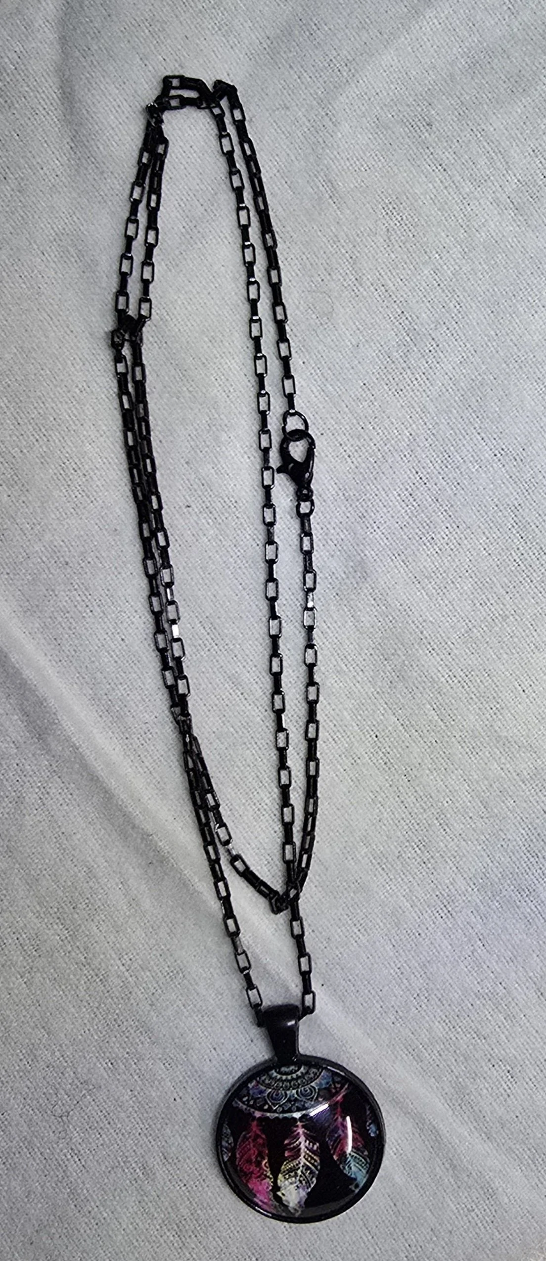 A black metal chain necklace with a round, colorful pendant featuring butterfly wings.