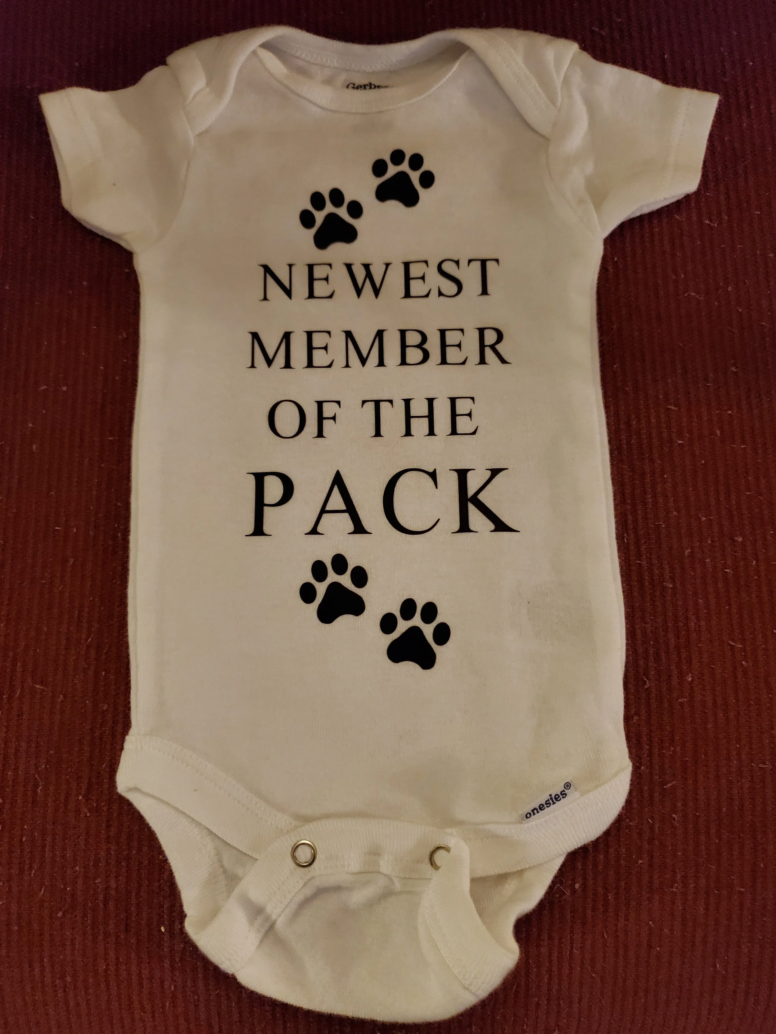 Baby onesie with printed text and paw prints, reading 'Newest Member of the Pack'.